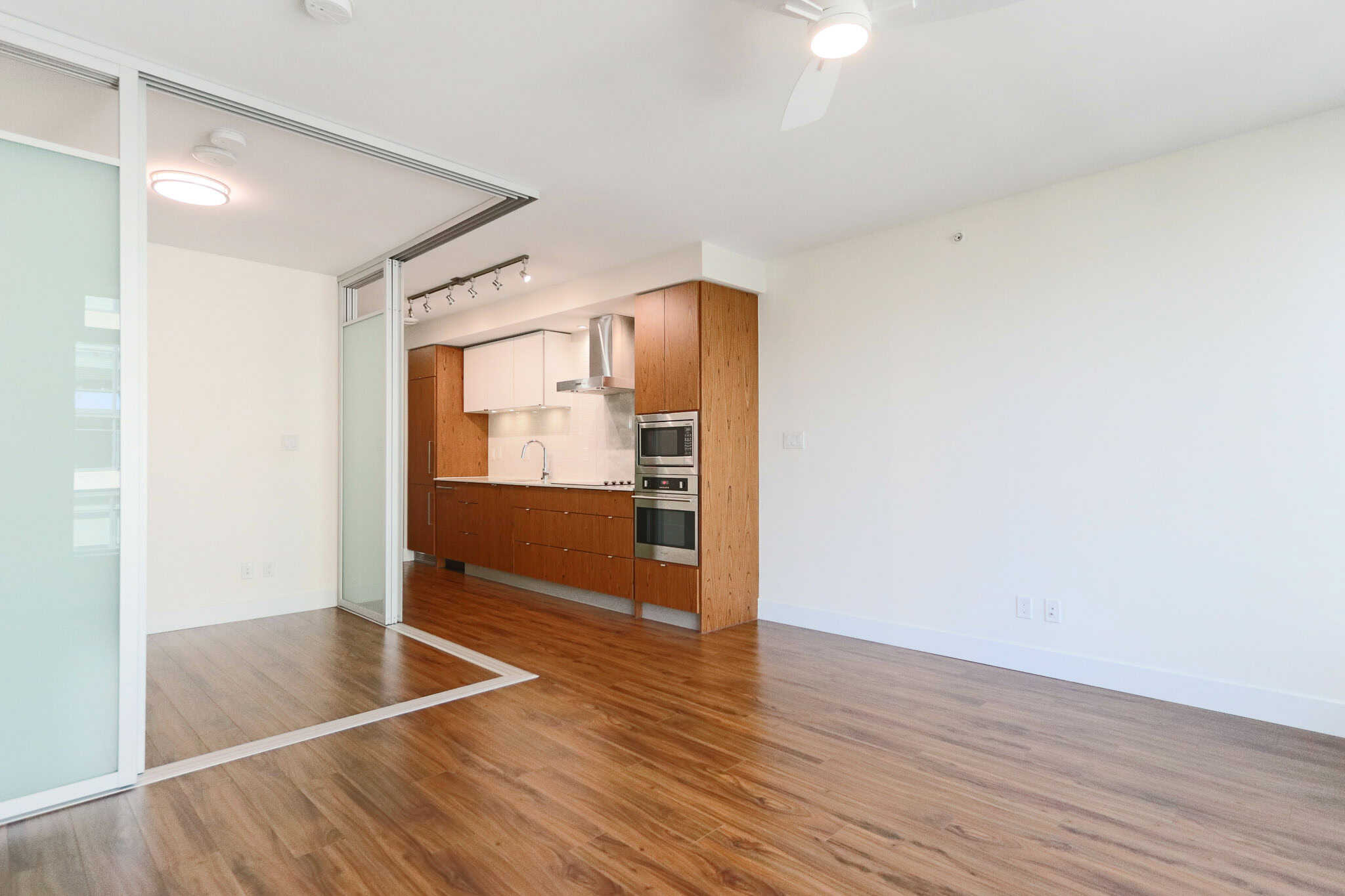 Contemporary open-concept kitchen and living space in a modern Vancouver condo, featuring hardwood floors, sleek cabinetry, and stainless steel appliances for stylish urban living.