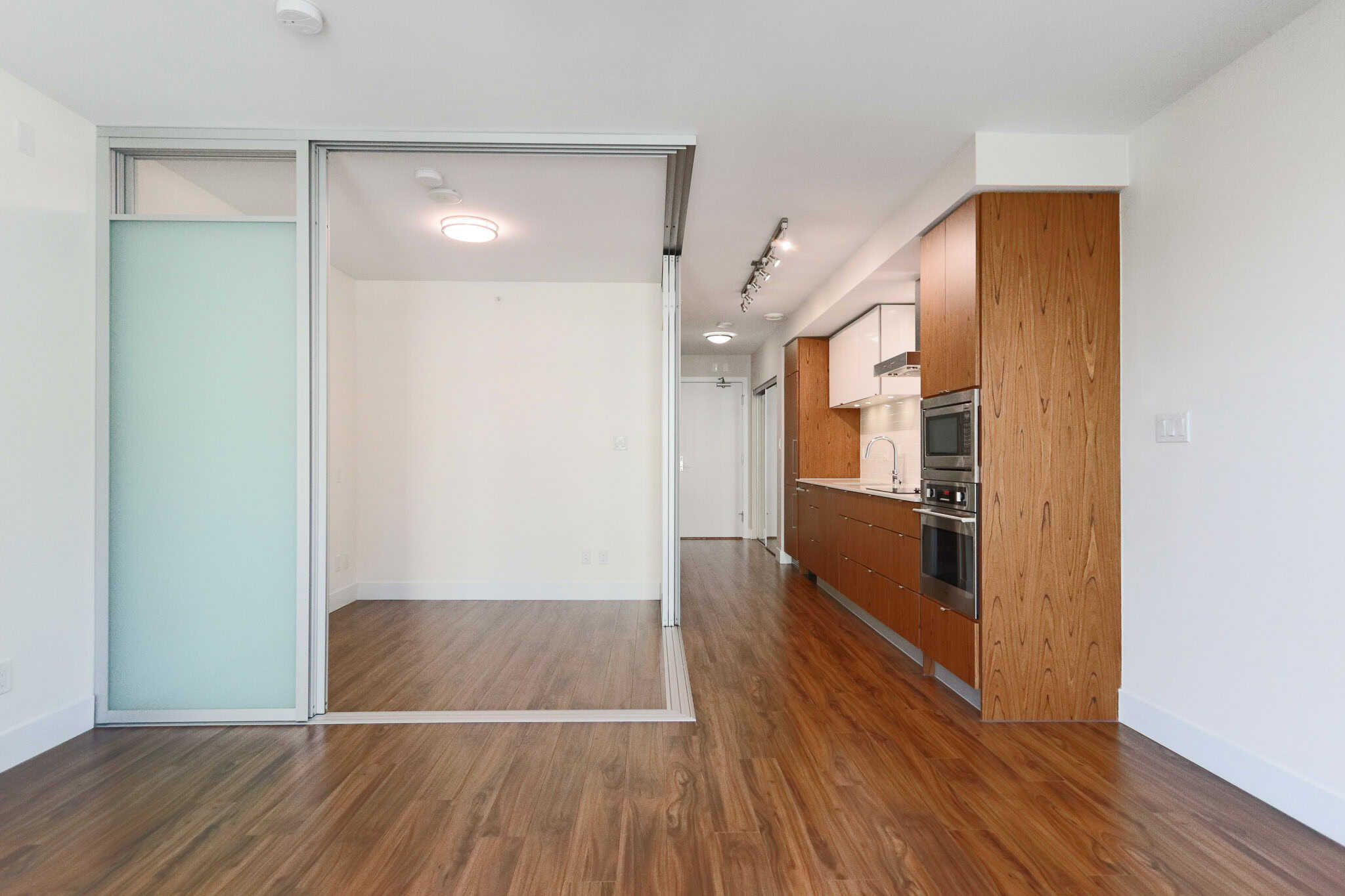 Bright modern open-concept apartment with wood flooring, sleek kitchen, and sliding frosted glass doors, ideal for Vancouver real estate investment and comfortable living.