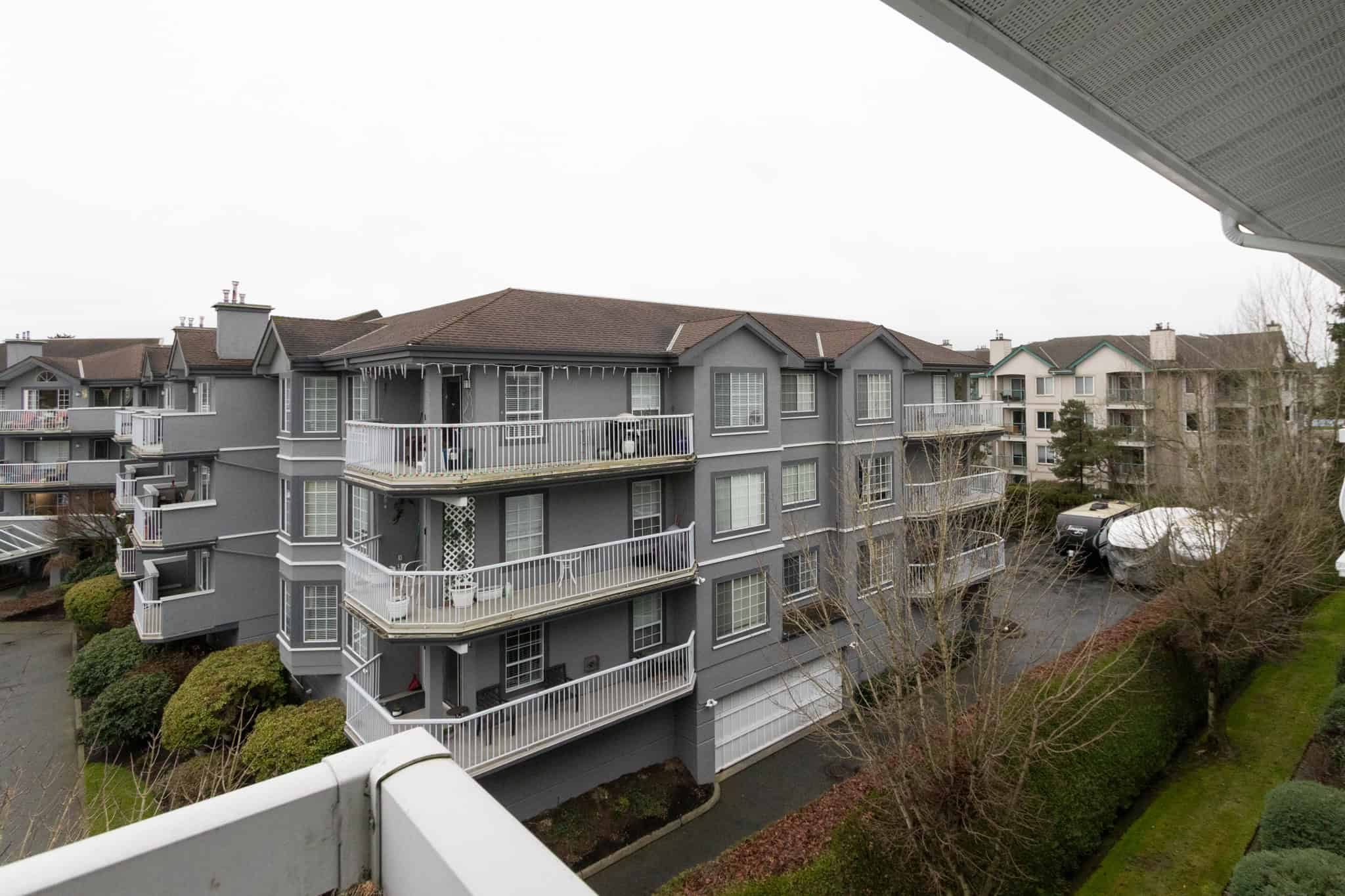 Spacious balcony view of a modern grey residential apartment complex in Vancouver, BC, showcasing outdoor living spaces, well-maintained landscaping, and a peaceful neighbourhood setting.