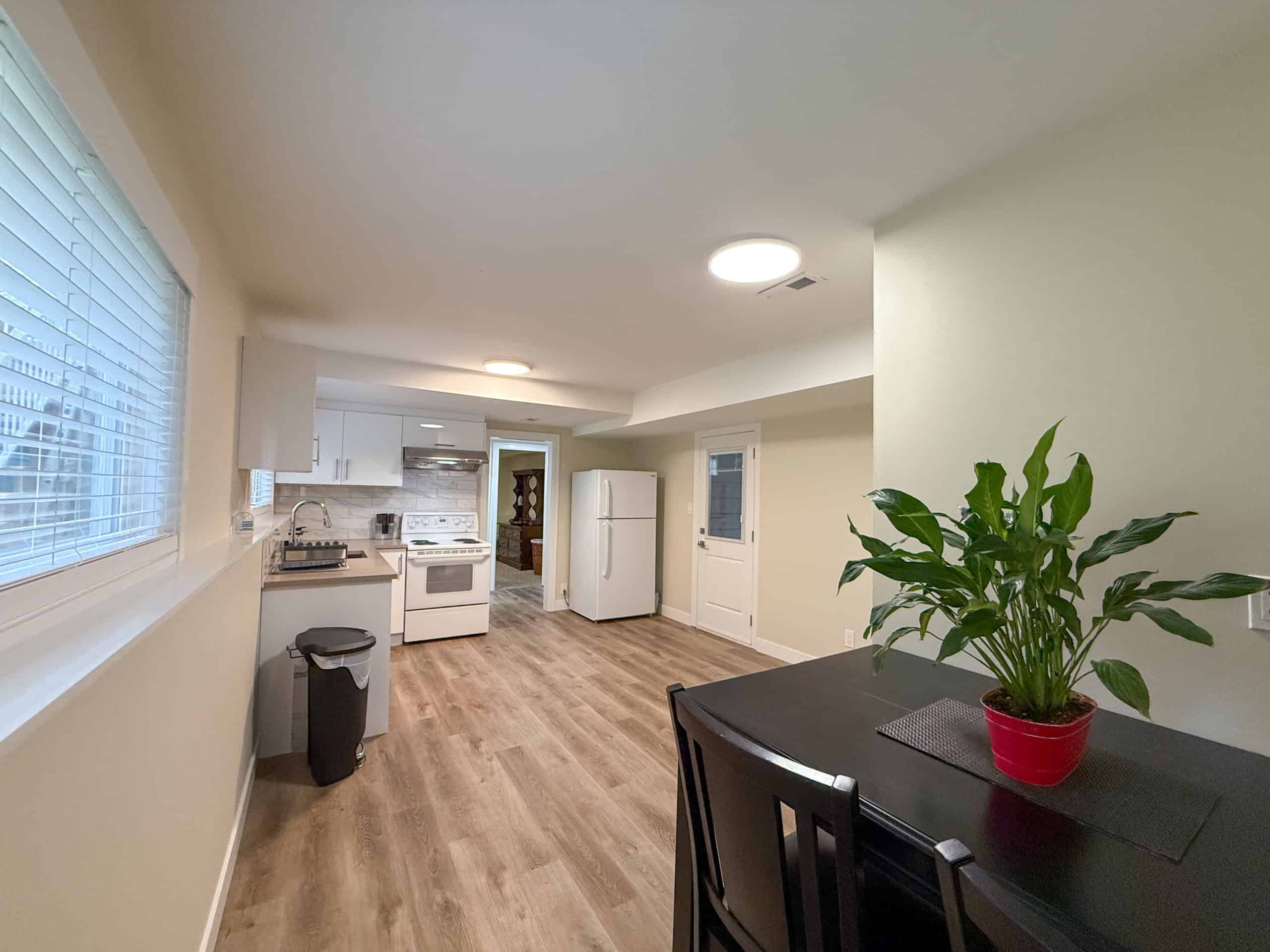 Bright and inviting kitchen with dining space in North Vancouver, featuring white cabinetry, modern appliances, and a potted plant for a fresh touch.