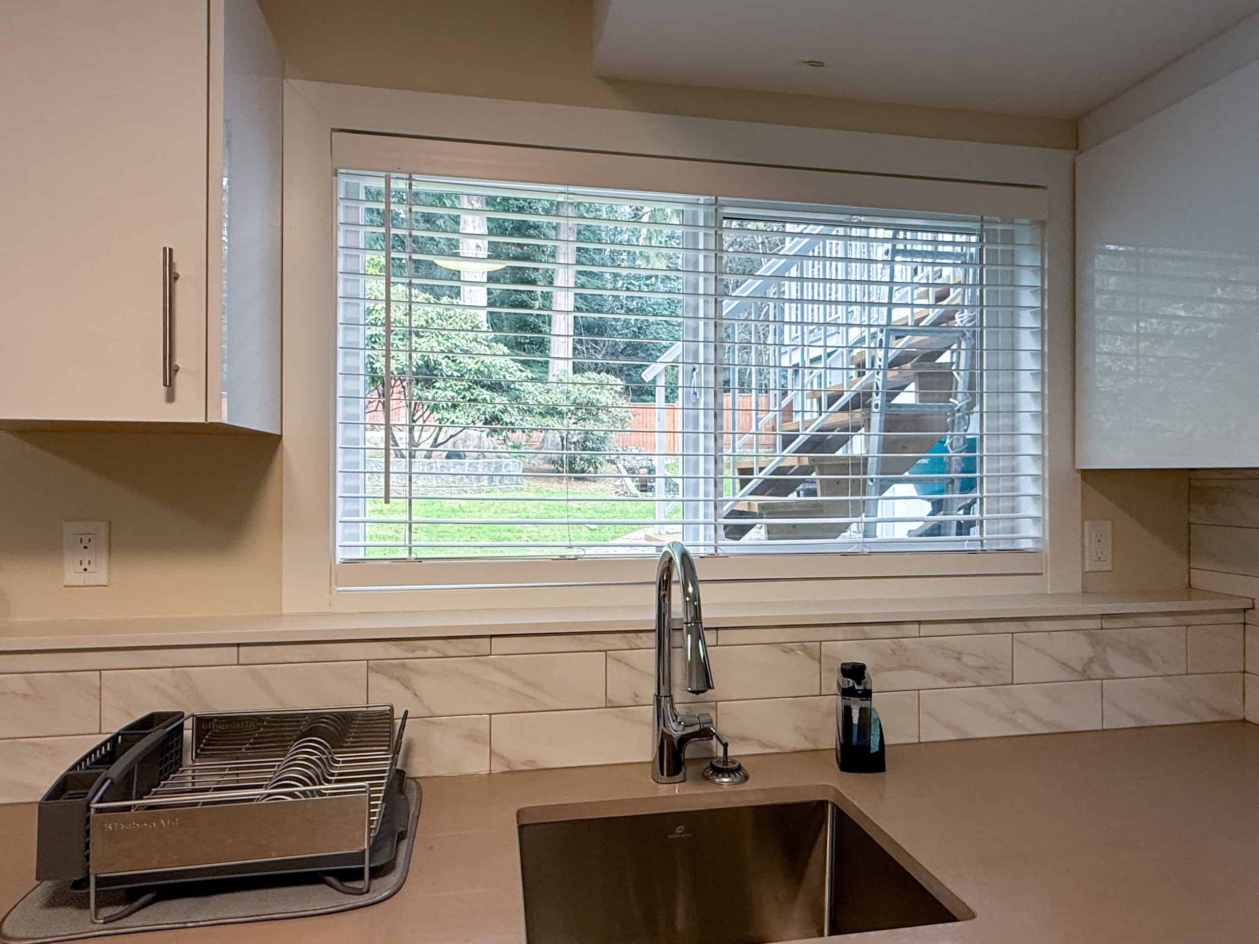 Bright kitchen with large window, stainless steel sink, and view of backyard and outdoor staircase.