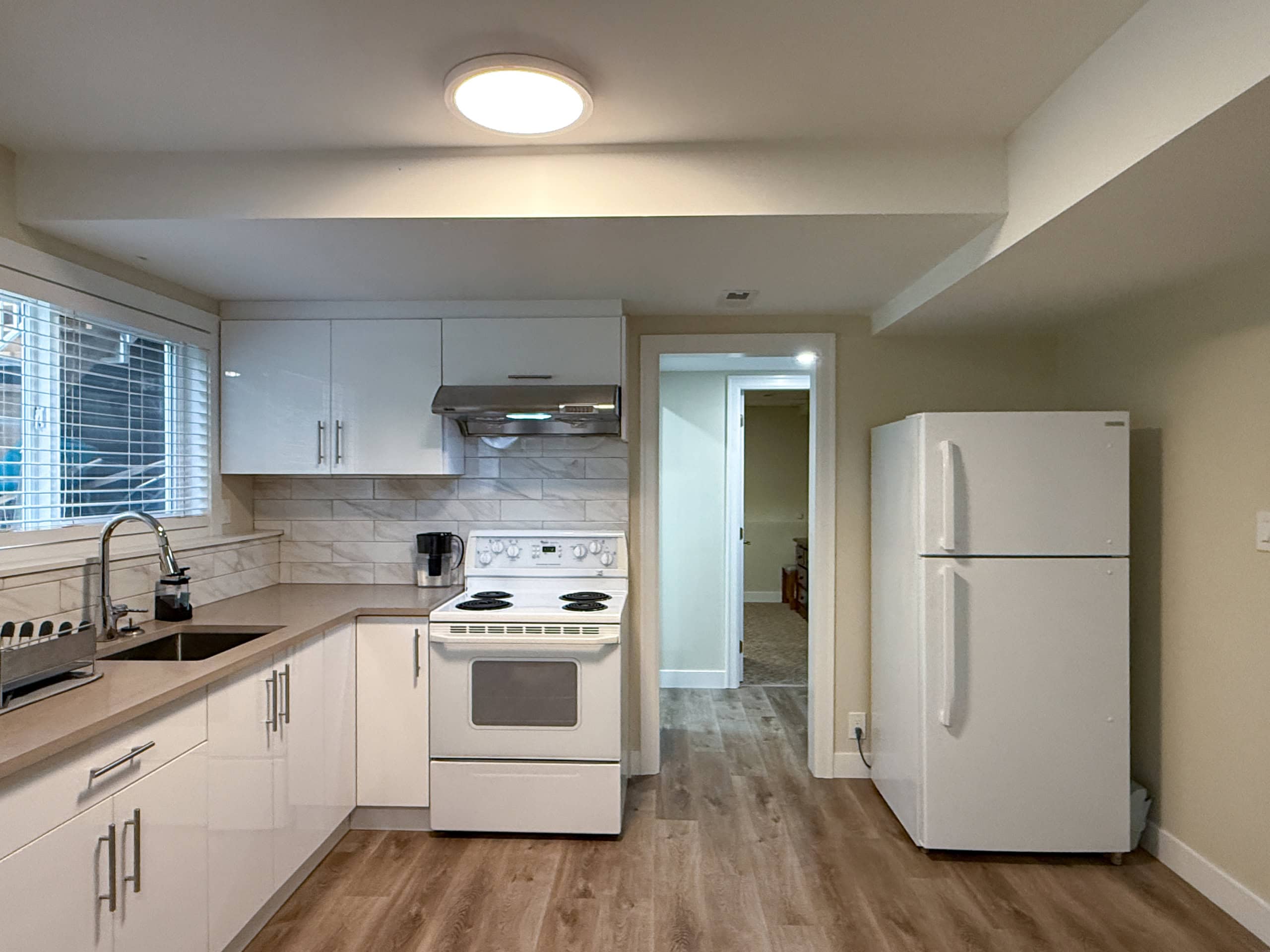 Modern kitchen in North Vancouver with white cabinetry, stainless steel appliances, and a large window providing natural light.