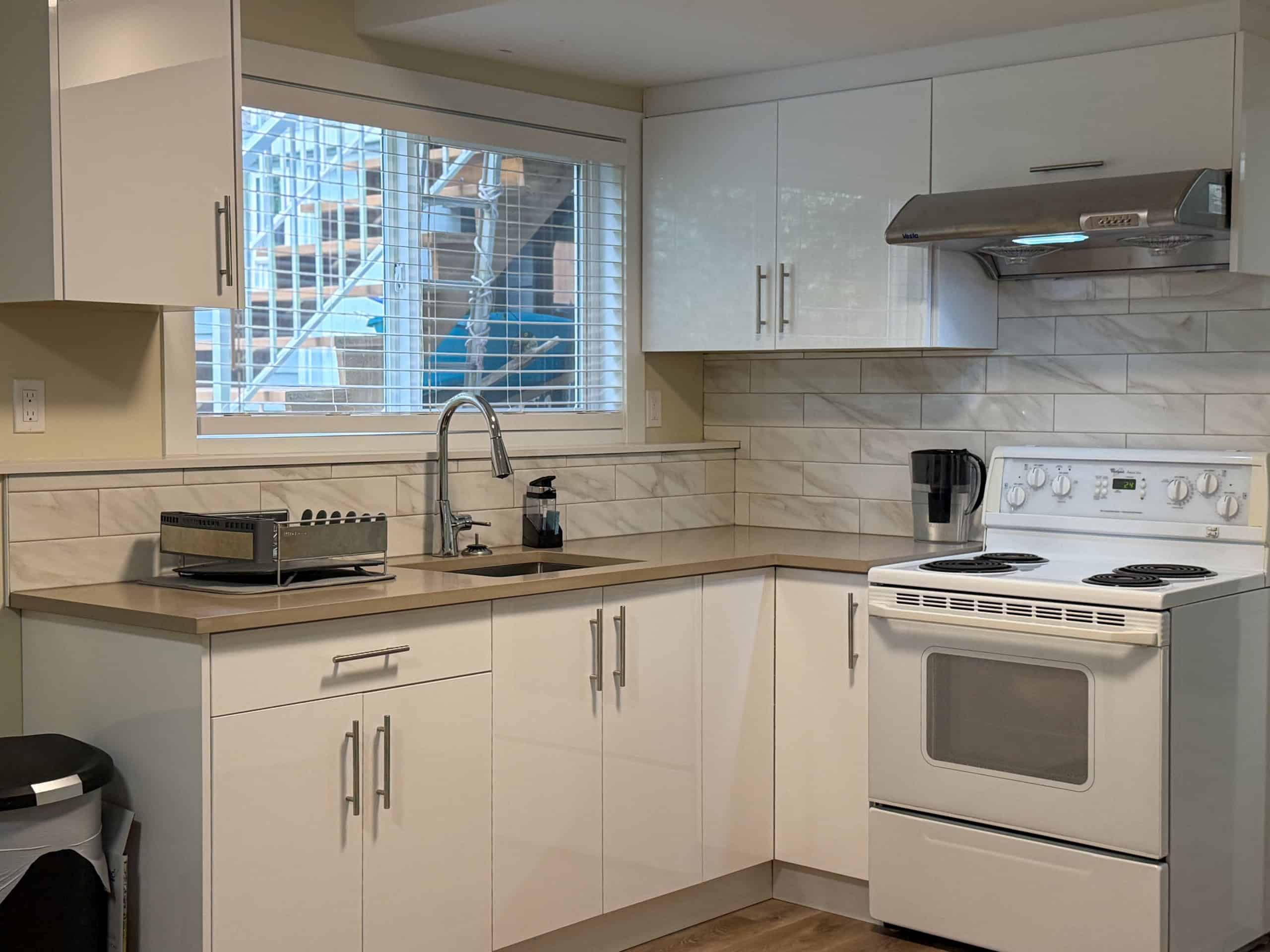 Bright kitchen featuring white cabinetry, a large window, and essential appliances in a North Vancouver home.