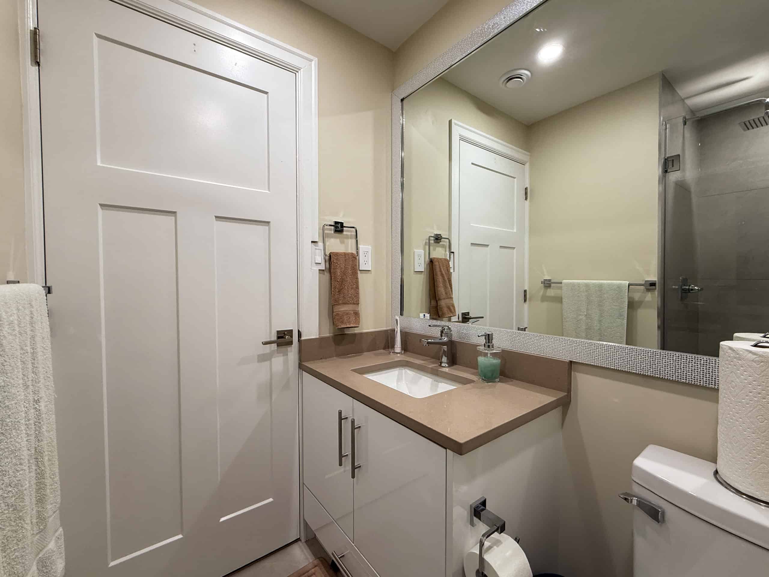 Bright, clean bathroom featuring a vanity with a large mirror, towel racks, and contemporary fixtures.