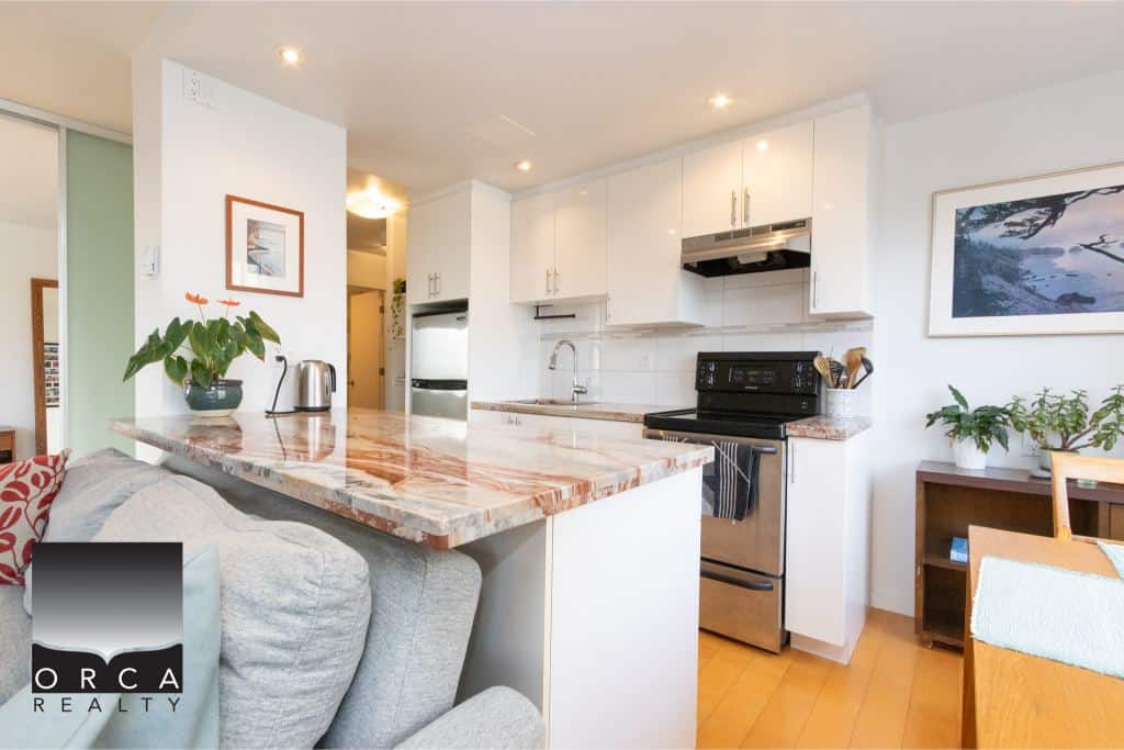 Modern kitchen with white cabinetry, stainless steel appliances, marble countertop, and cozy dining area – perfect for homebuyers seeking a stylish urban property in Canada.