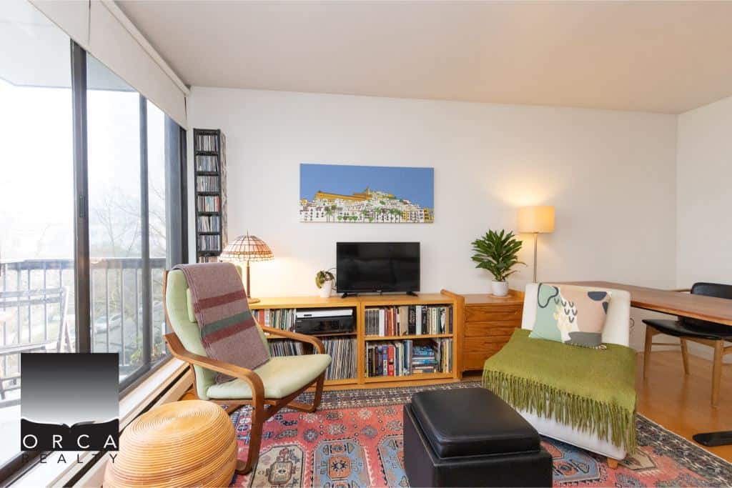 Cozy living room with modern decor, large window for natural light, wooden furniture, and a mix of artwork and plants, perfect for Vancouver real estate enthusiasts.
