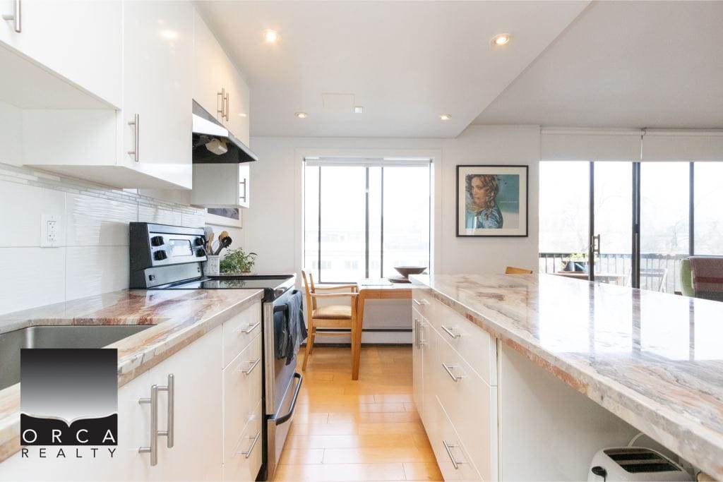 Bright modern kitchen with white cabinetry, granite countertops, stainless steel appliances, and large windows showcasing city views – ideal for Vancouver real estate.
