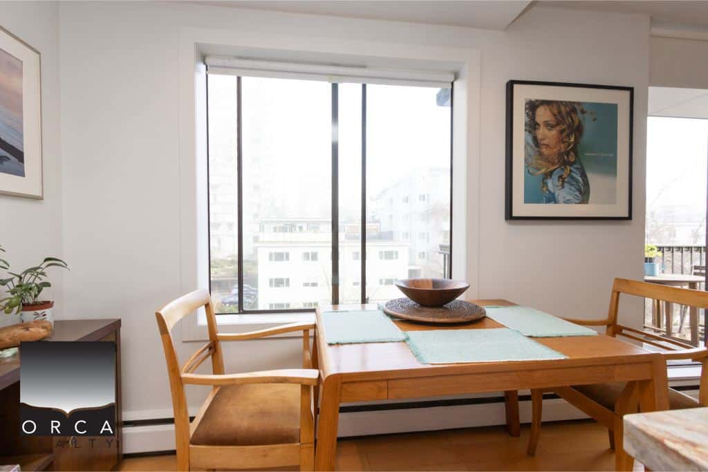 Bright dining room with large window overlooking cityscape, modern decor, and wooden furniture, ideal for Vancouver real estate buyers seeking style and comfort, part of Orca Realty Inc.'s property listings.