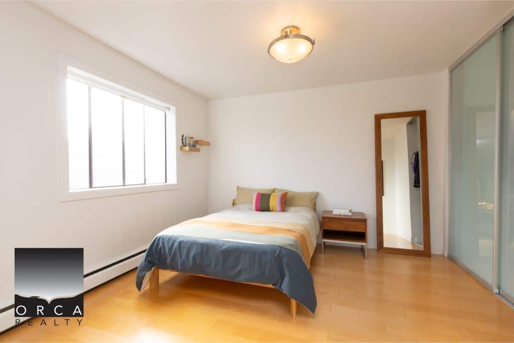Bright bedroom with spacious minimalist design, featuring a large window, wooden flooring, and modern decor, ideal for Vancouver real estate buyers seeking stylish, comfortable homes in the region.