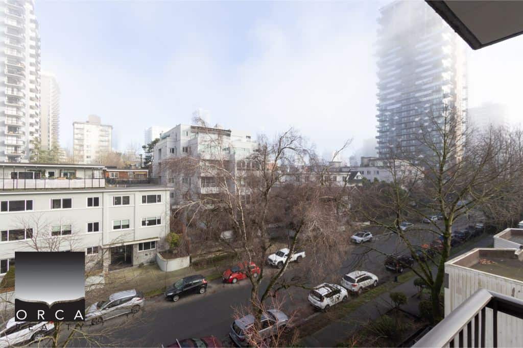 Modern urban view of downtown Vancouver from an apartment balcony, showcasing high-rise buildings, tree-lined streets, and parked cars, perfect for Vancouver real estate and property investment.