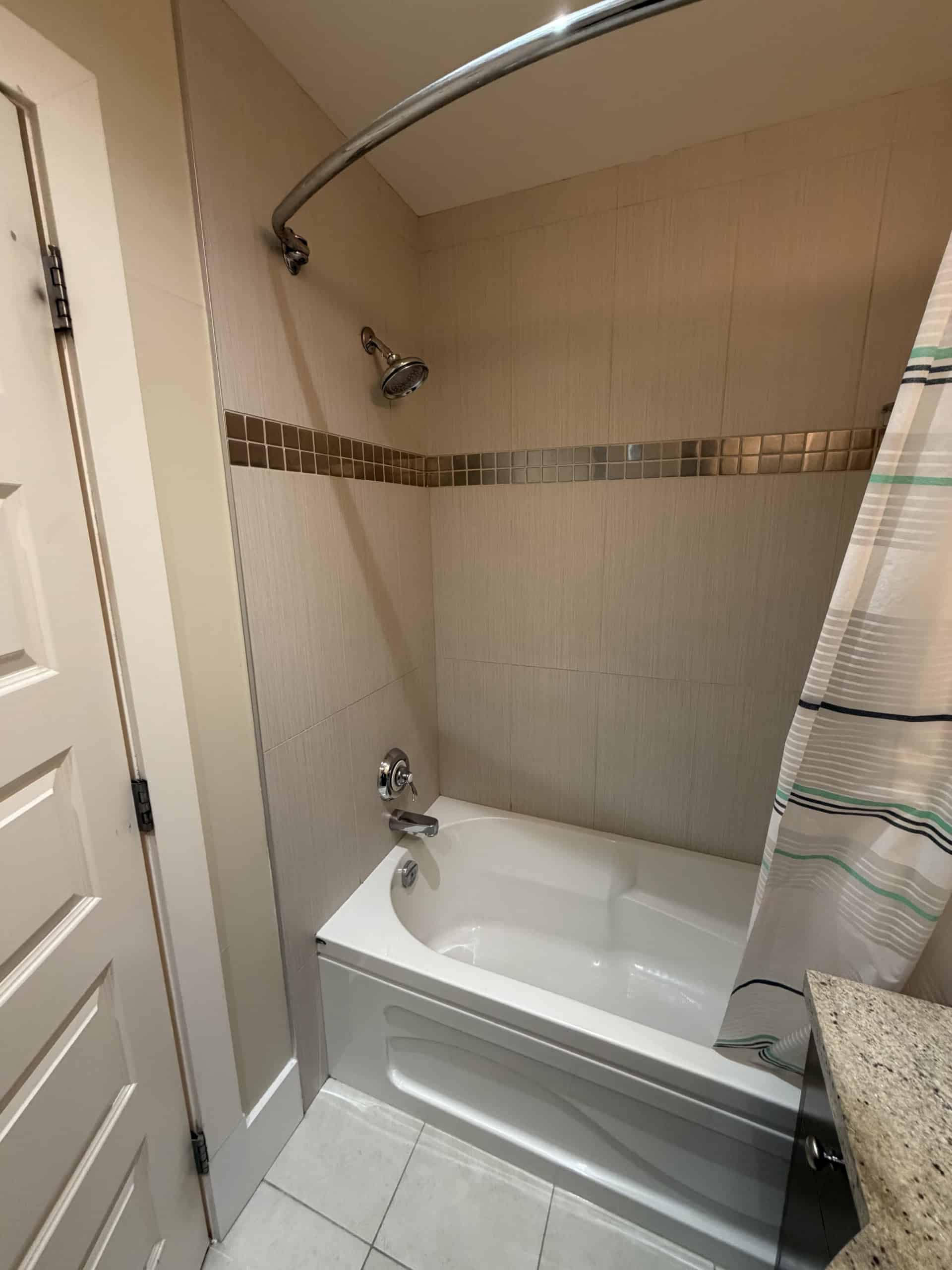 Modern bathroom shower with bathtub, beige tiled walls, and a shower curtain, perfect for comfortable family living or rental properties in BC.