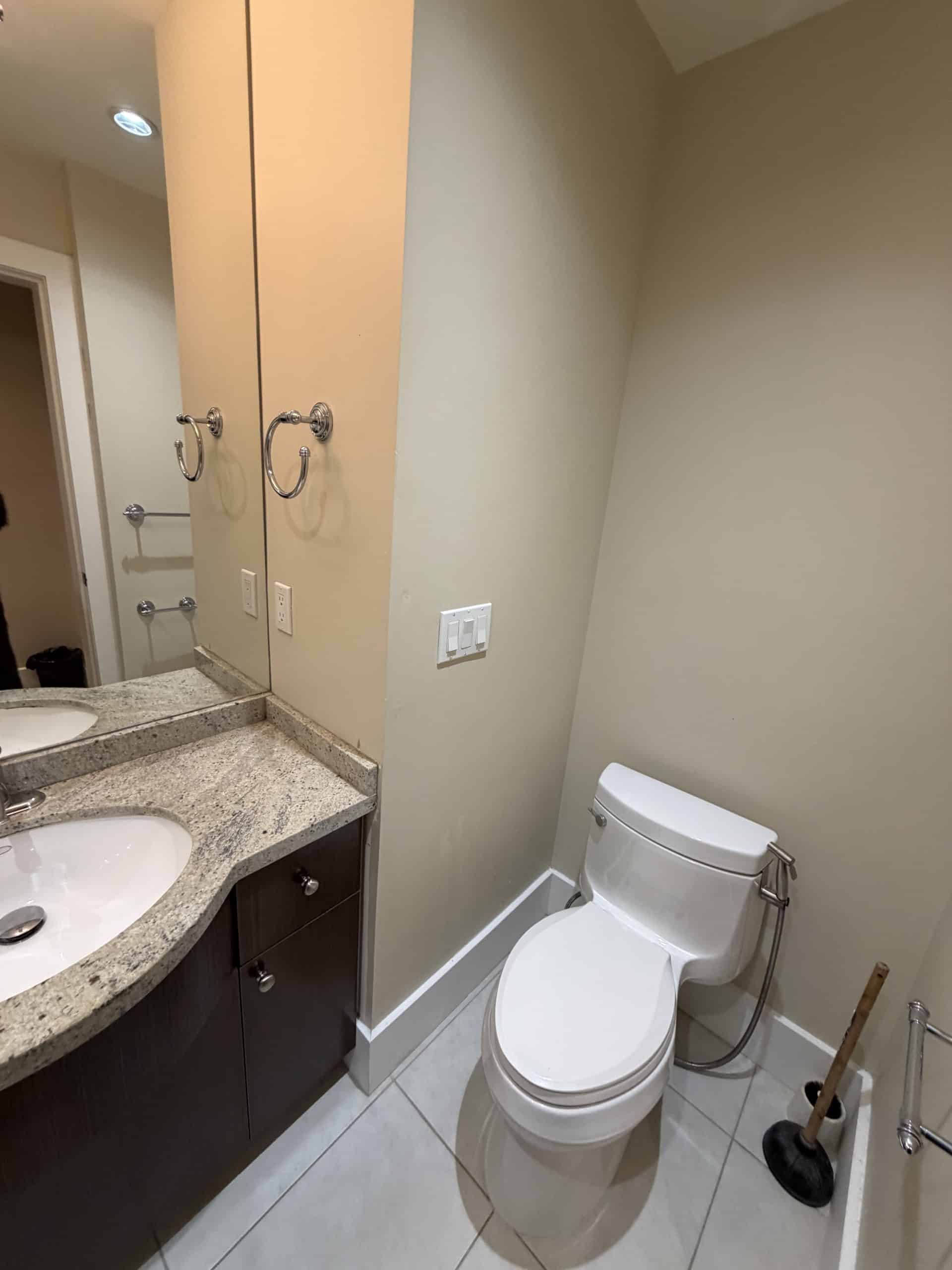 Contemporary bathroom with modern granite vanity, dual sinks, and sleek fixtures. Features a comfortable toilet and ample space, perfect for stylish and functional home living. Ideal for real estate listings.