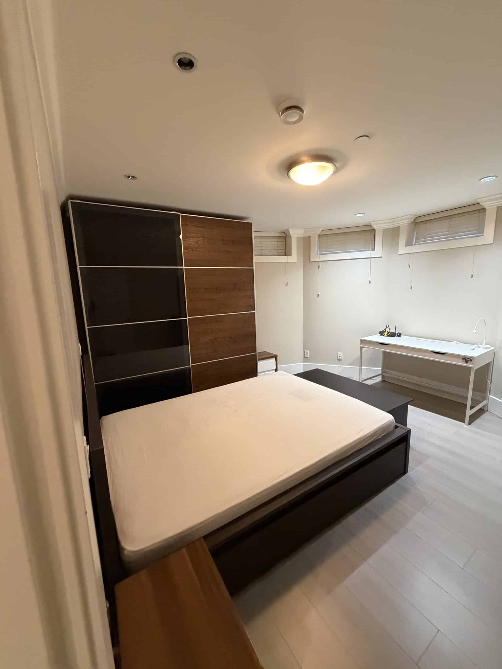 Modern bedroom featuring a minimalist design with a sleek black and wood-paneled wardrobe, white mattress, and contemporary furnishings; ideal for Vancouver and Victoria real estate markets.