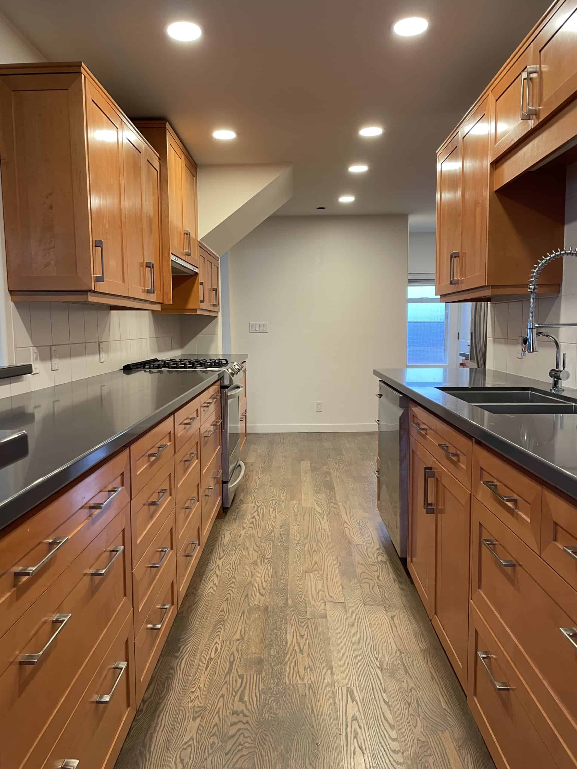 Warm wood kitchen cabinets with modern black countertops and stainless steel appliances, featuring recessed lighting, perfect for Vancouver Island real estate.