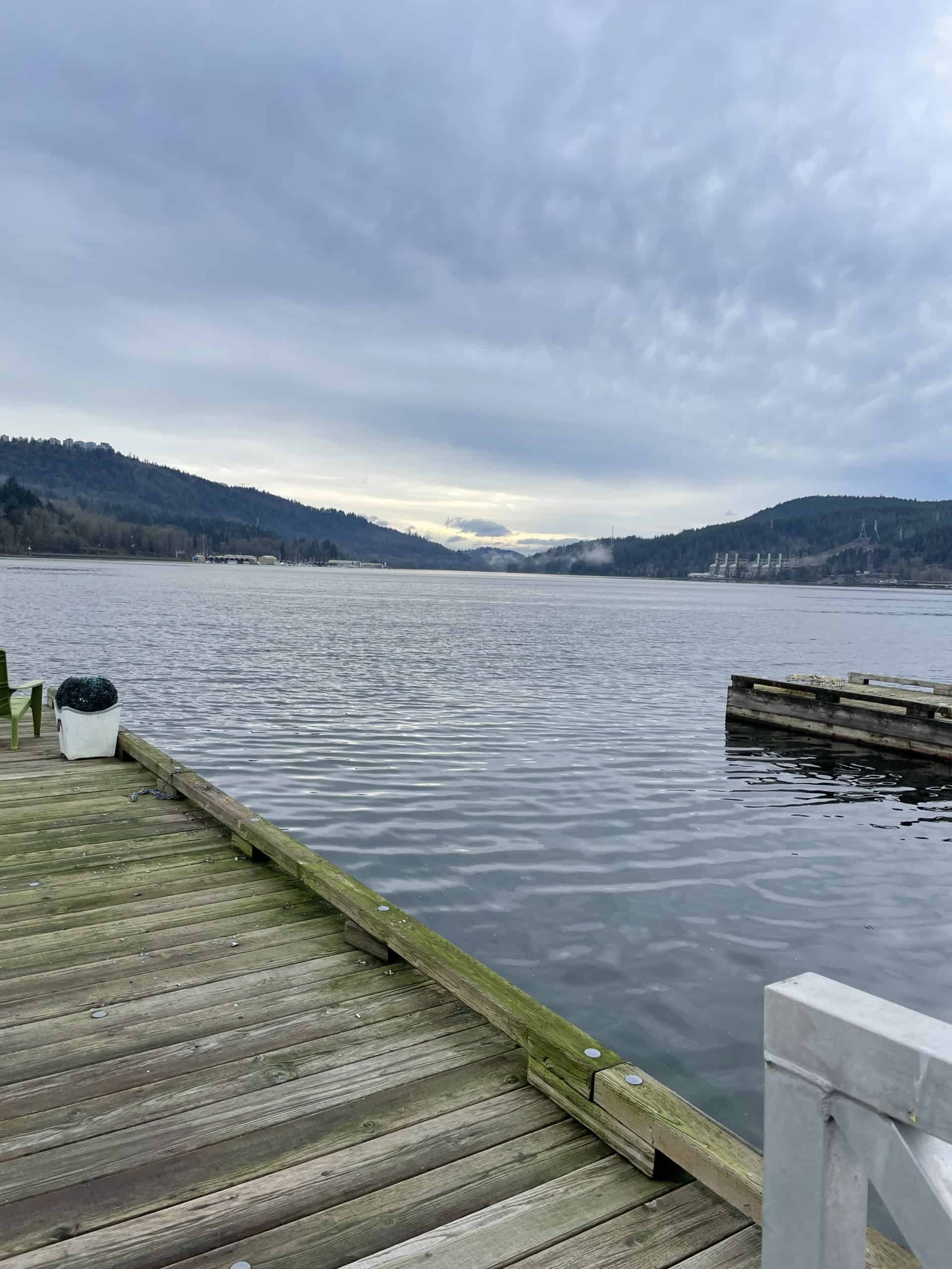 Serene lakeside view from a wooden dock, showcasing calm water, surrounding mountains, and cloudy skies, ideal for waterfront property listings by Orca Realty Inc. in British Columbia.