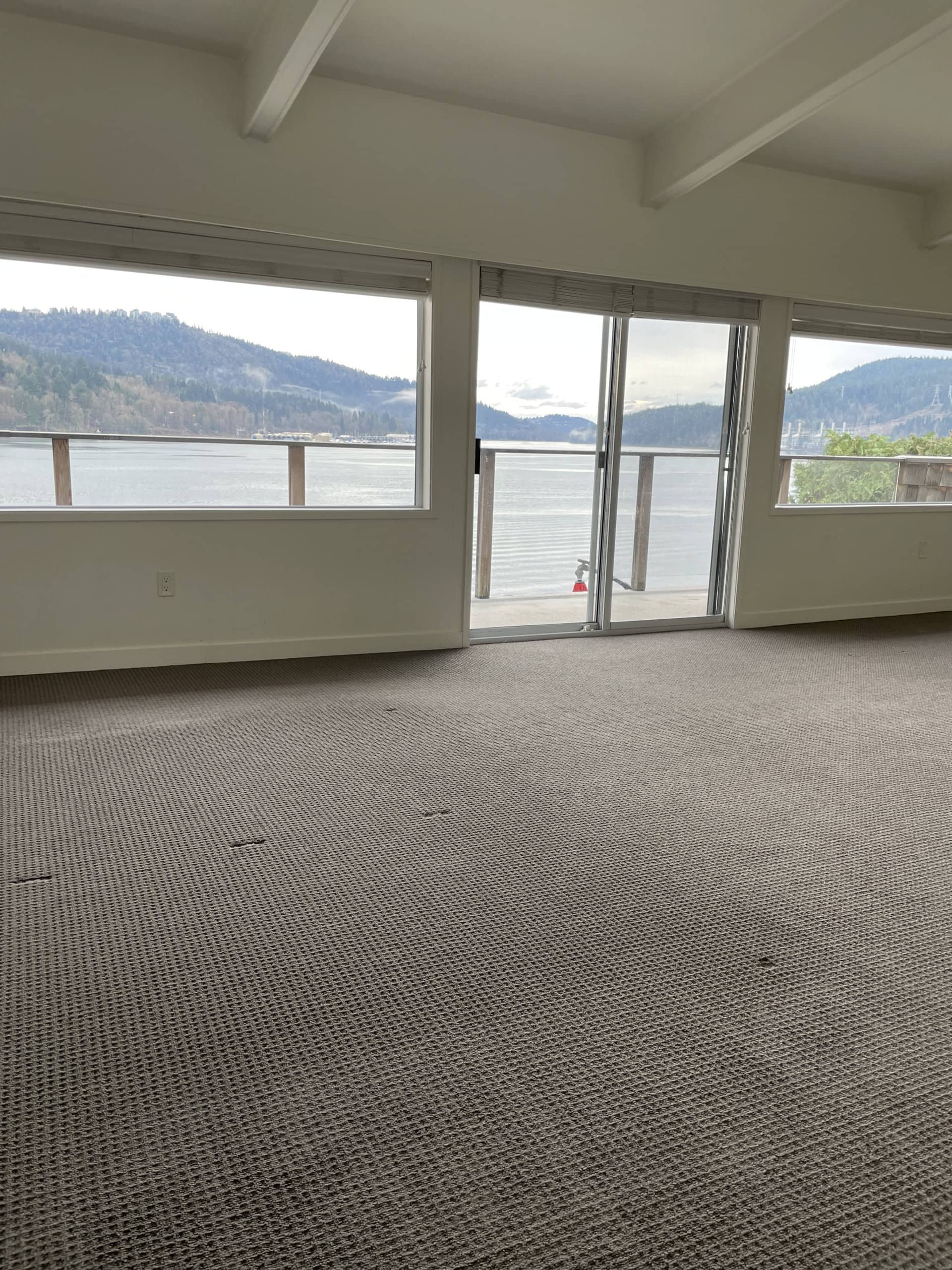 Spacious waterfront living room with large windows and balcony, offering stunning mountain and lake views, perfect for relaxation and enjoying natural scenery in Orca Realty Inc. listings.