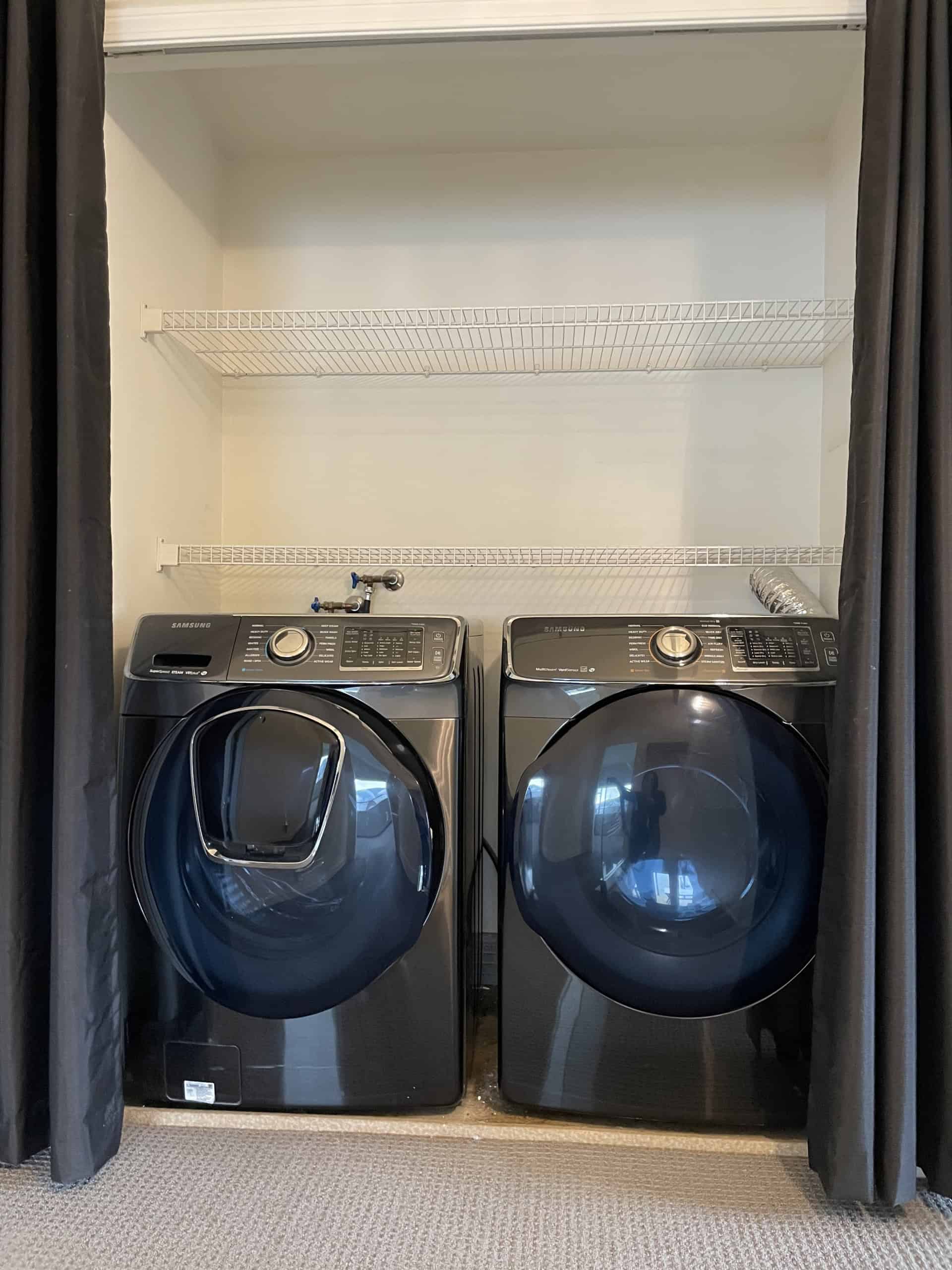 Modern laundry room with black front-load washer and dryer, white wire shelving, and neutral decor, showcasing practical home utility space, ideal for Vancouver Island real estate listings and property marketing.