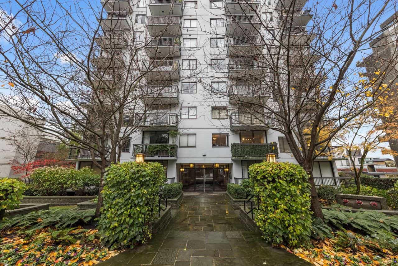 Modern high-rise condo building entrance with landscaped garden and trees, showcasing Vancouver real estate opportunities.