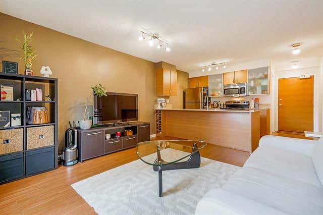 Bright and modern interior of a Vancouver condo at 309-928 Homer St, featuring an open-plan living room with a white sofa, glass coffee table, and a well-equipped kitchen.