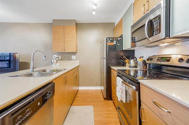 Bright and functional kitchen in Vancouver featuring stainless steel refrigerator, oven, microwave, and dishwasher, with ample wooden cabinetry and a spacious countertop for cooking and entertaining.