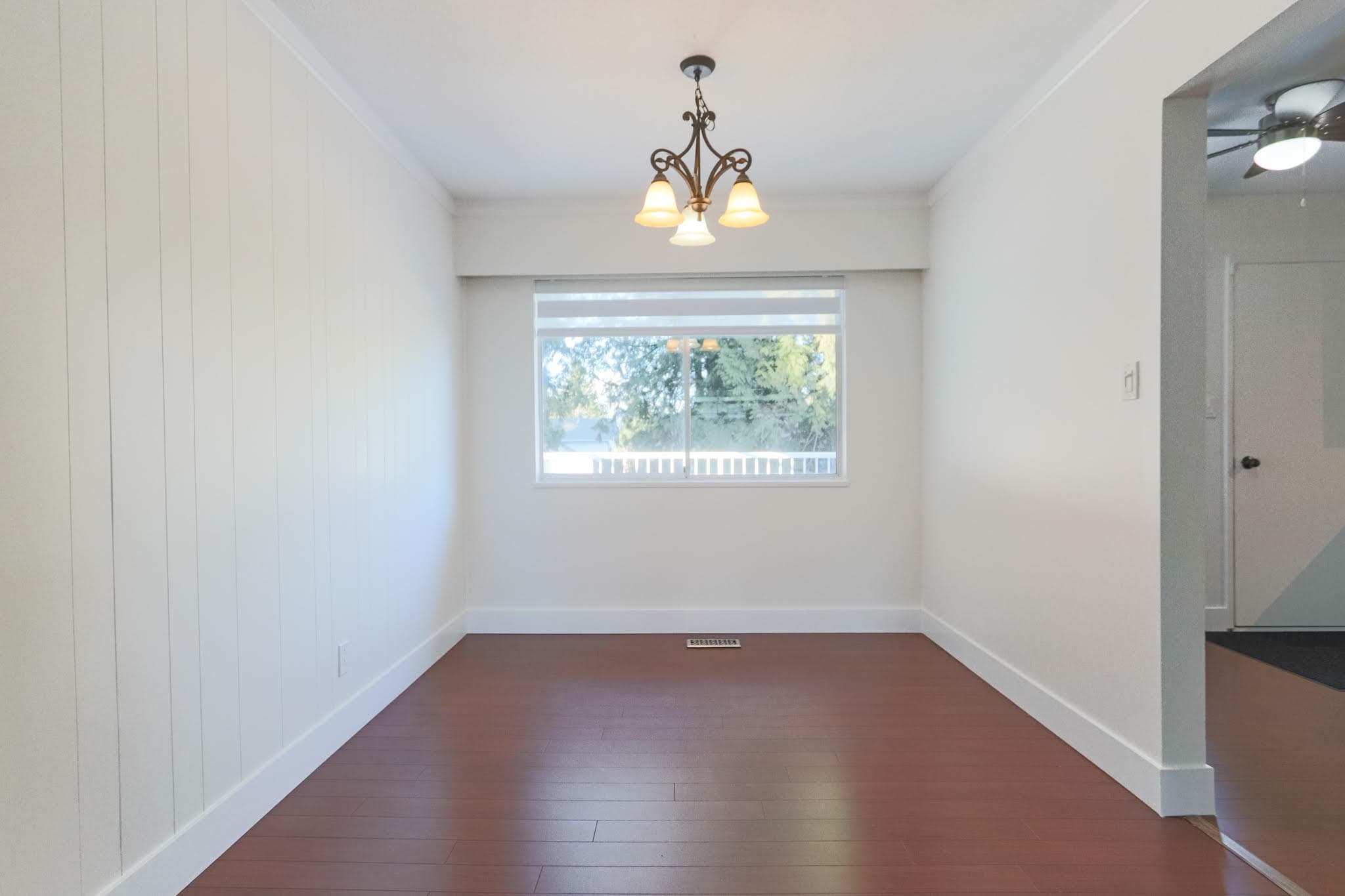 Upstairs room in a residential property at 10833 85A Avenue, Delta, featuring a large window, hardwood flooring, and a ceiling light fixture, ideal for living or dining space.