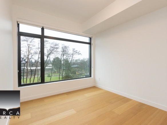 Bright, empty room in Vancouver condo with large window overlooking green trees, hardwood flooring, and white walls, ideal for home staging or real estate listings.