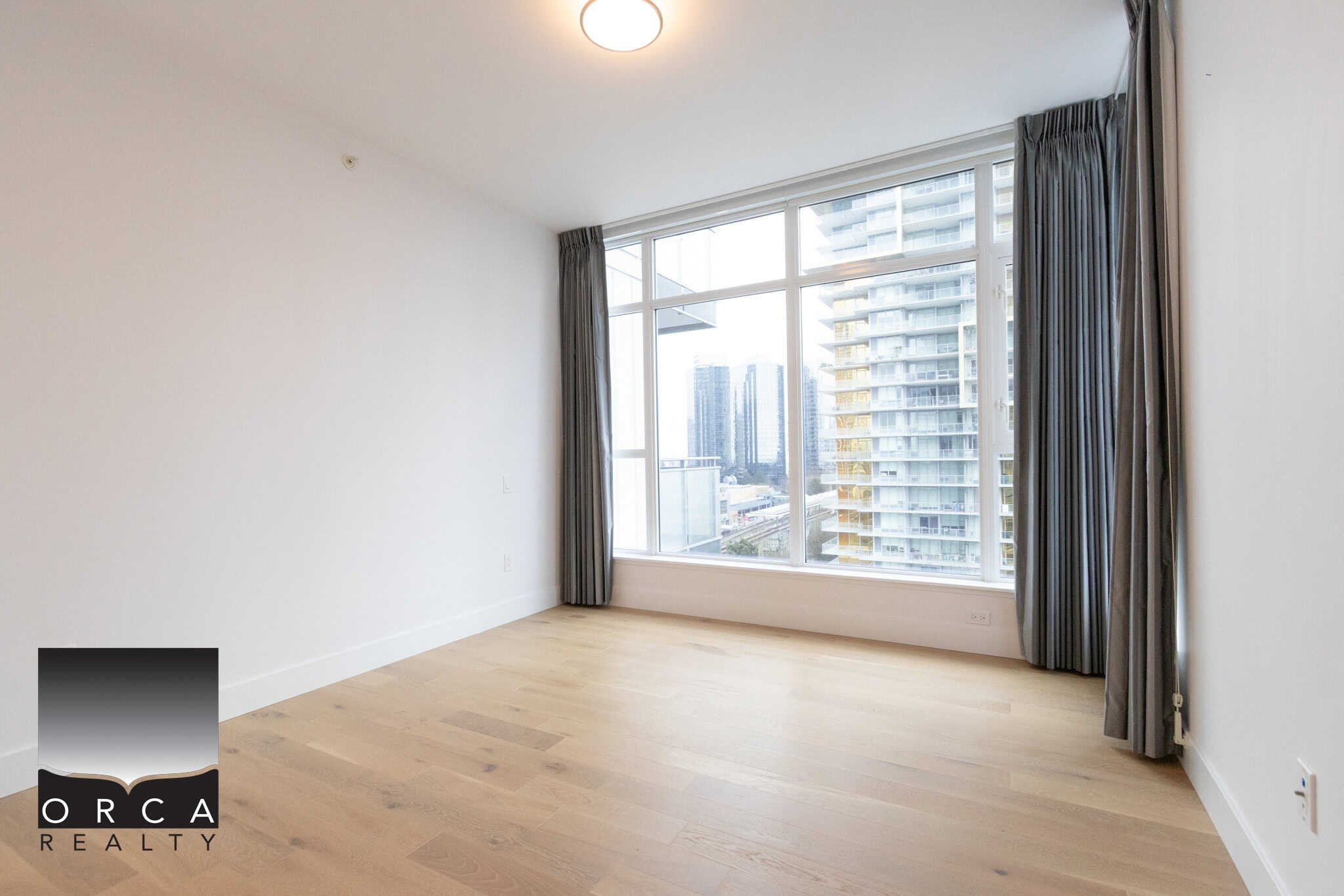 Spacious Vancouver condo featuring a large window with panoramic city views, hardwood floors, and natural light, perfect for comfortable urban living in the 1106-4360 Beresford Street area.