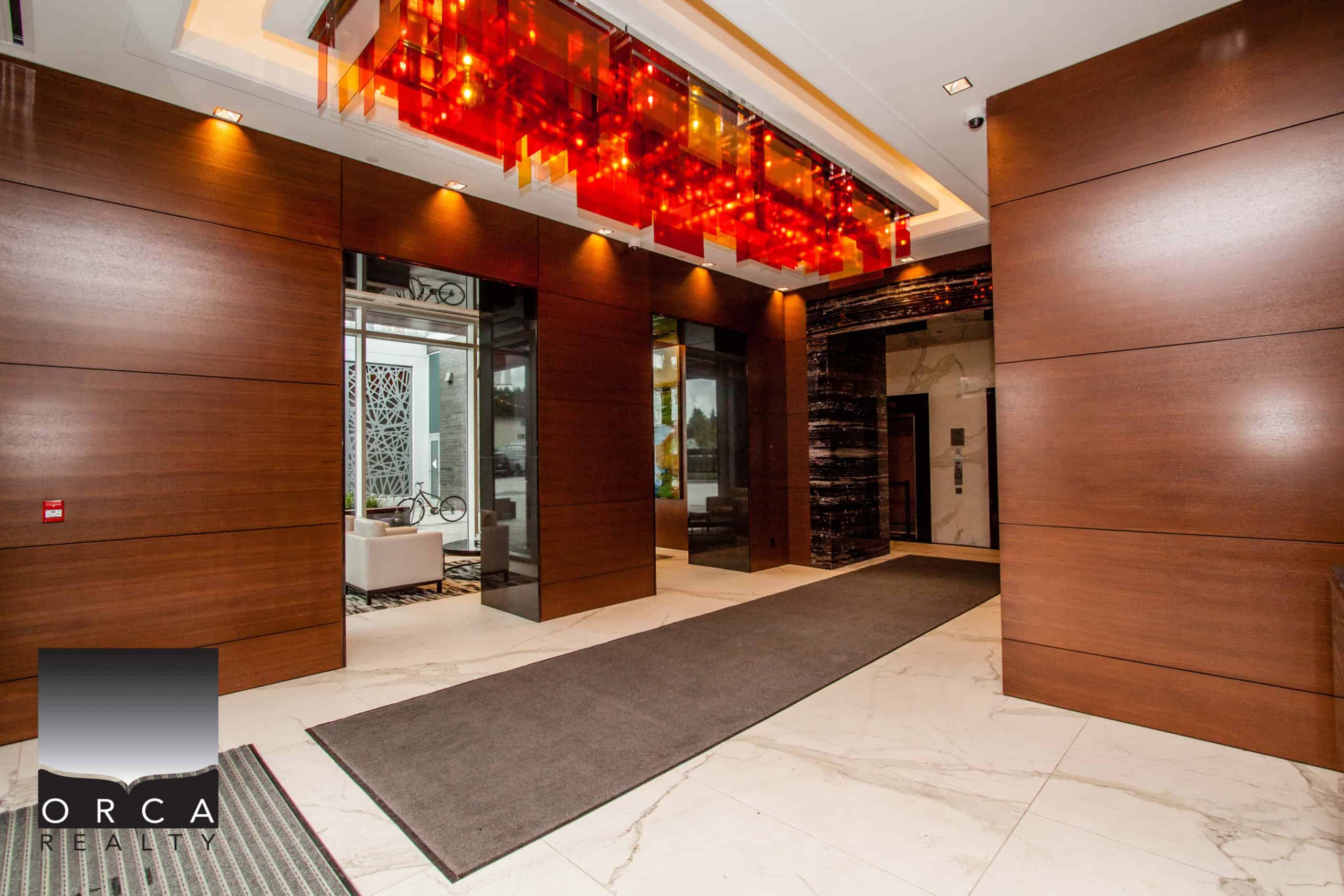Elegant condo building entrance featuring warm wood paneling, polished marble floors, and contemporary design elements.