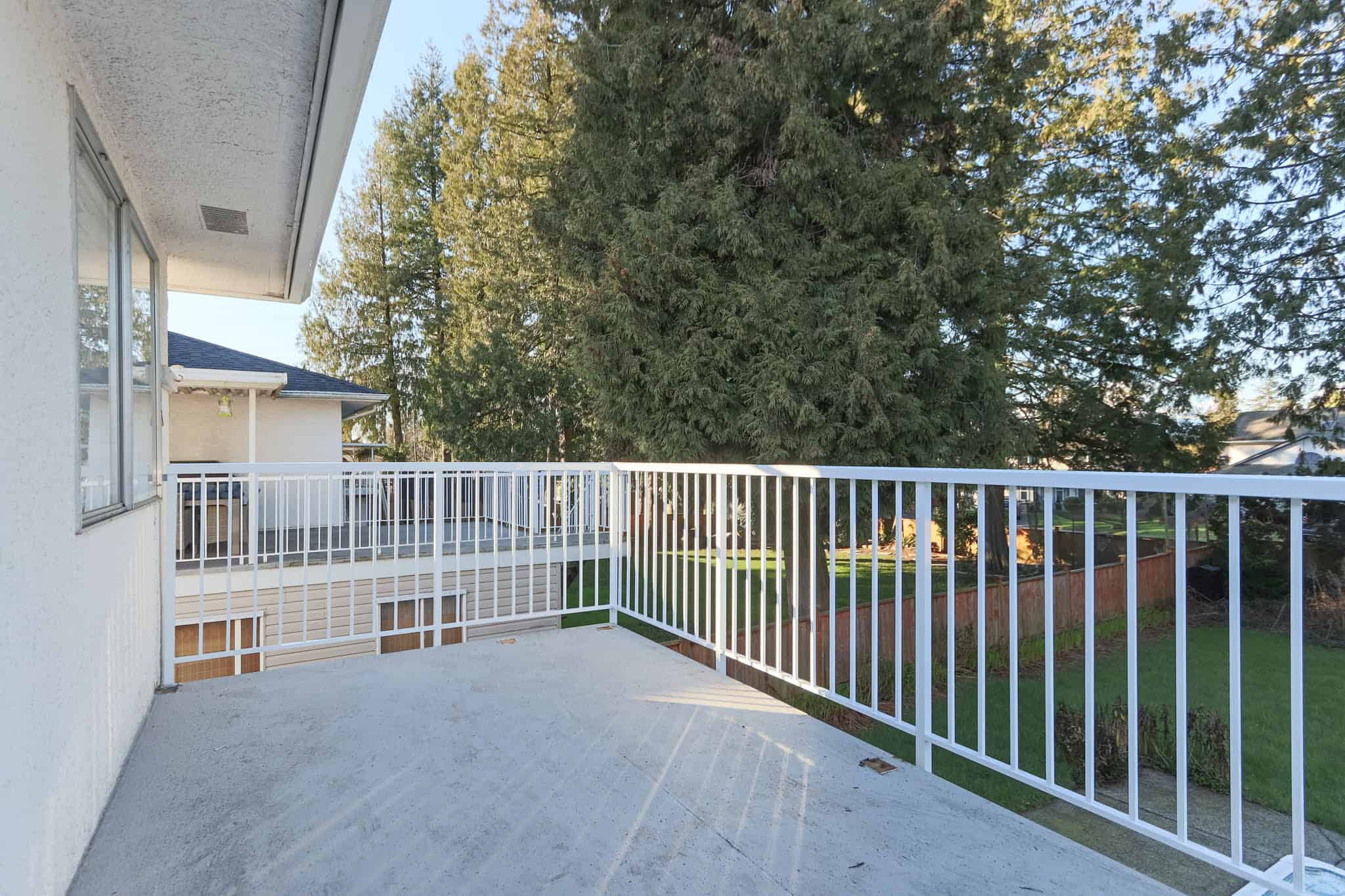 Upstairs balcony view at 10833 85A Avenue, Delta, showcasing a private outdoor space with a white railing, overlooking lush greenery and mature trees. Perfect for relaxing or outdoor activities.