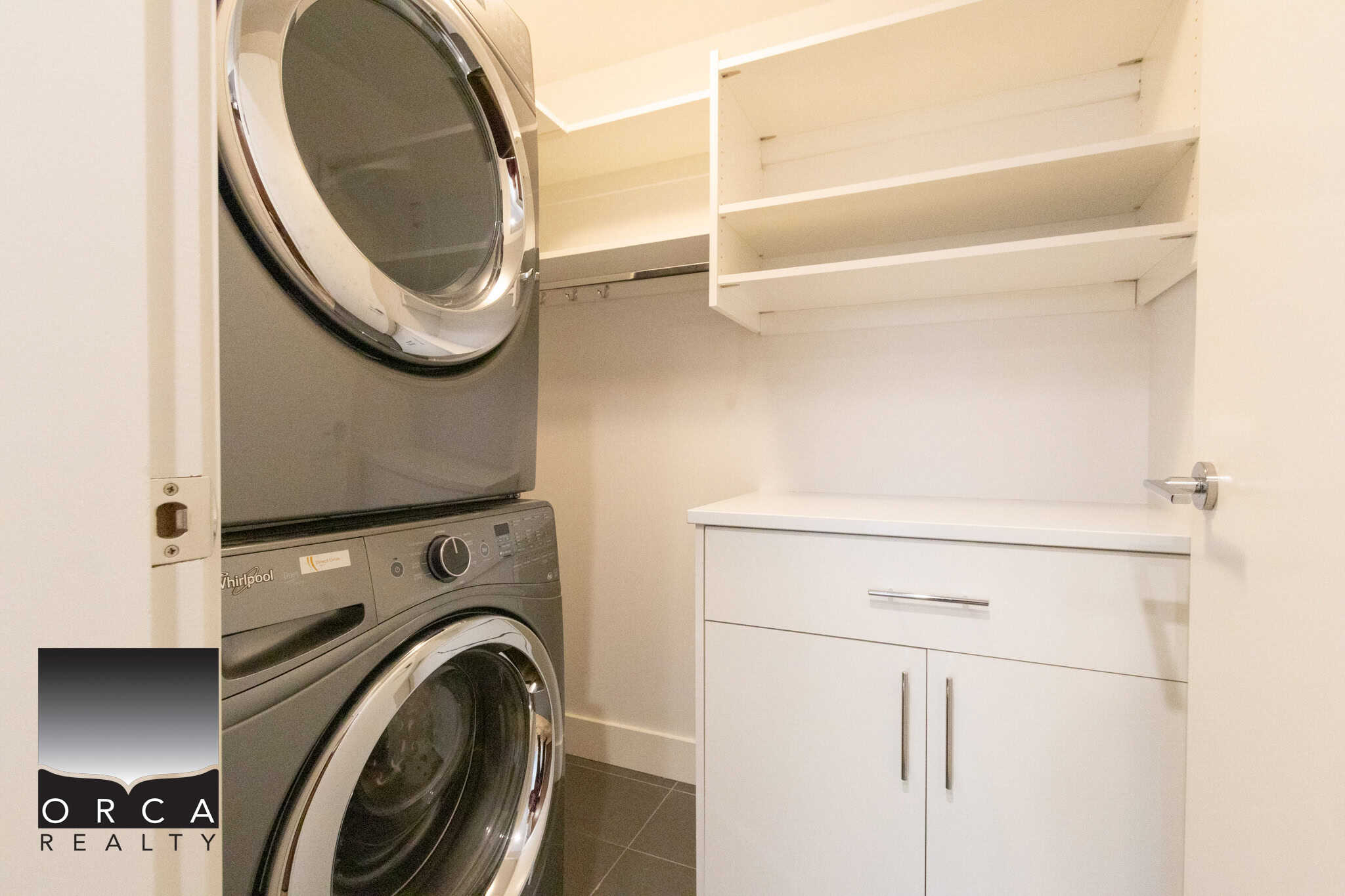 Bright laundry area featuring stacked washer and dryer units with storage shelves in a Vancouver residence.