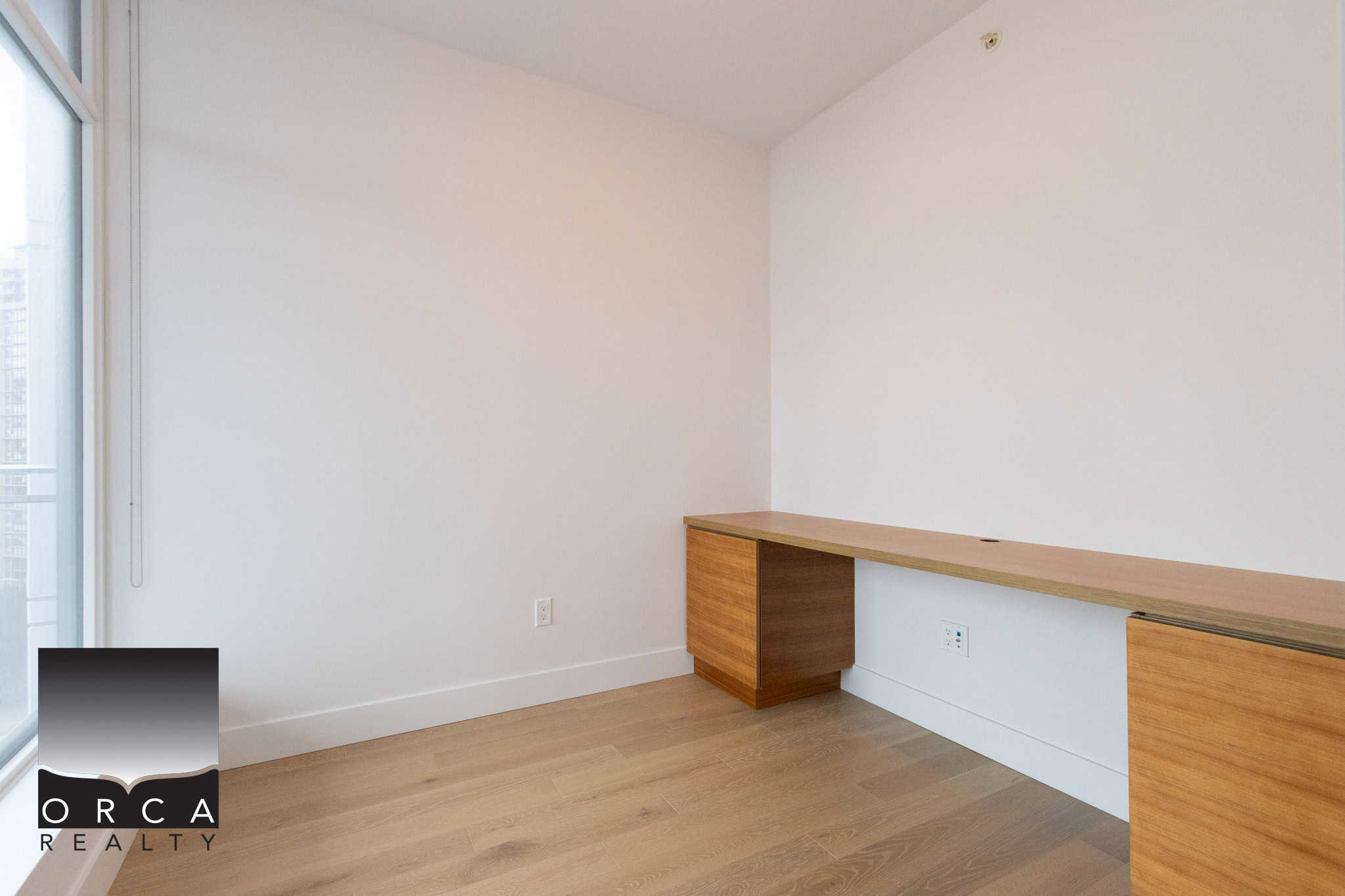 Bright, minimalist office room in Vancouver with white walls, wooden flooring, and built-in desk area, ideal for professional work environments.