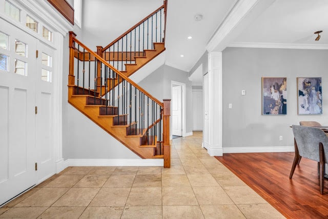 Bright and spacious entryway of a West Vancouver home with a wooden staircase, tiled flooring, and contemporary decor, showcasing elegant interior design.