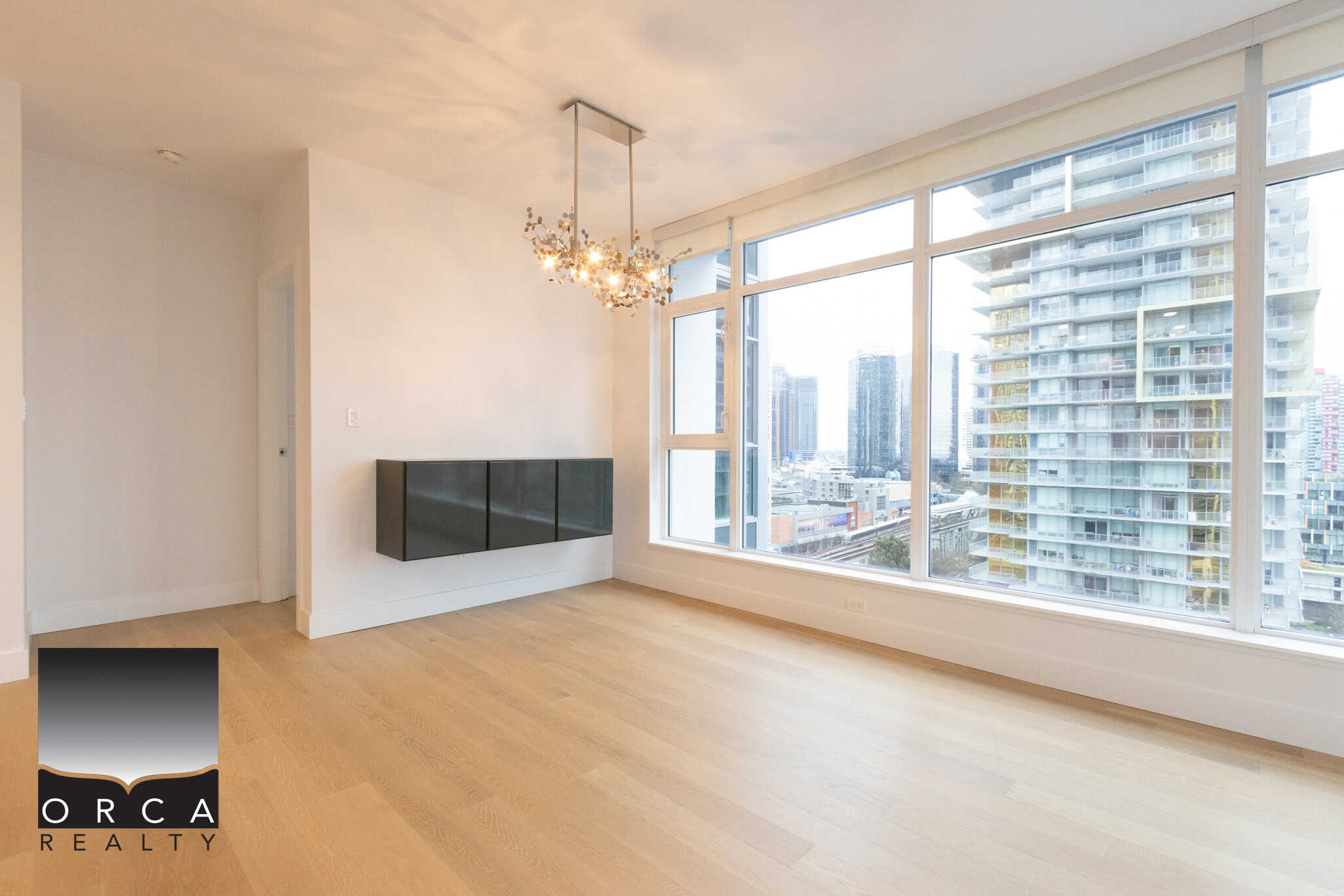 Bright, spacious living room in a downtown Vancouver apartment with large windows showcasing cityscape and high-rise buildings.