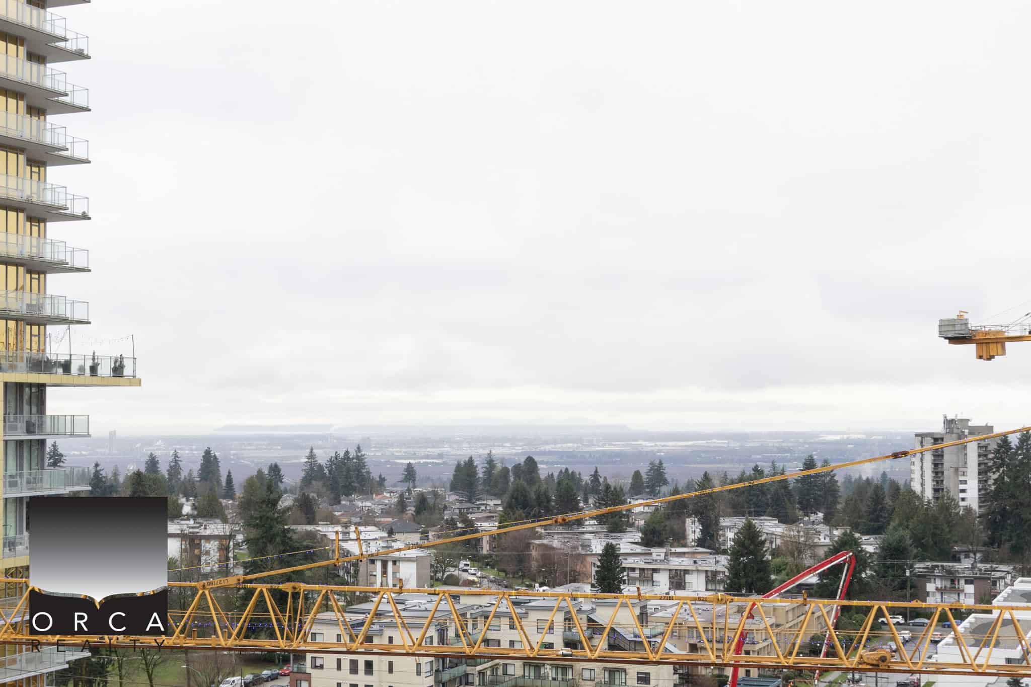 Construction crane overlooking Vancouver residential area with cityscape and distant mountains.