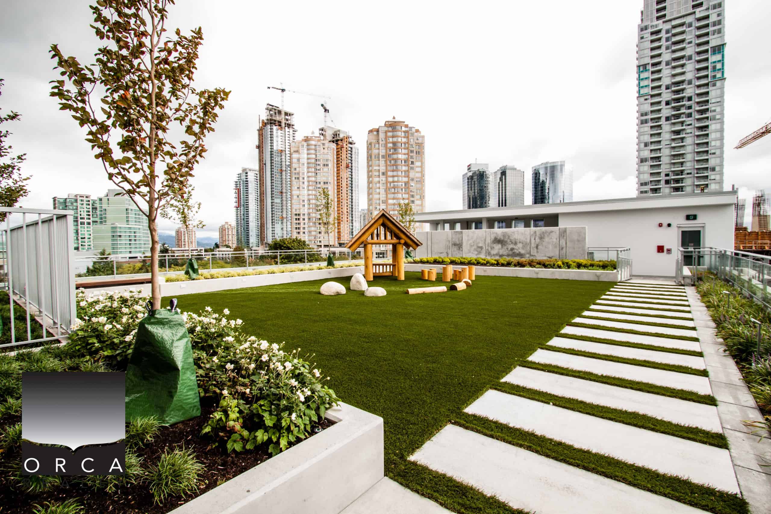 Rooftop garden at 1106-4360 Beresford Street, Vancouver, featuring lush green grass, a wooden playhouse, and contemporary landscaping with city skyscrapers in the background.