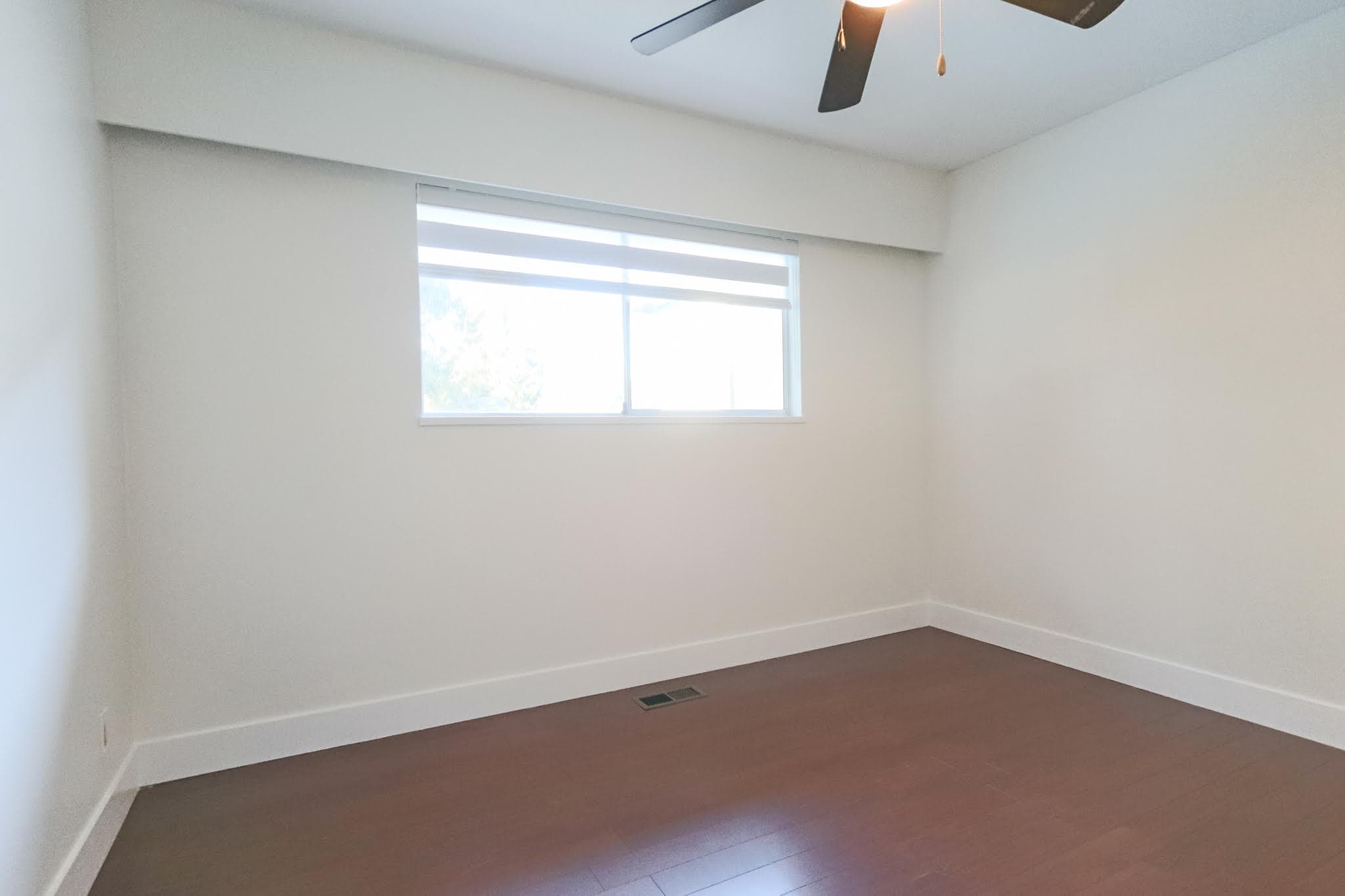 Upstairs room in Delta home with large window, white walls, and ceiling fan, ideal for bedroom or office space.