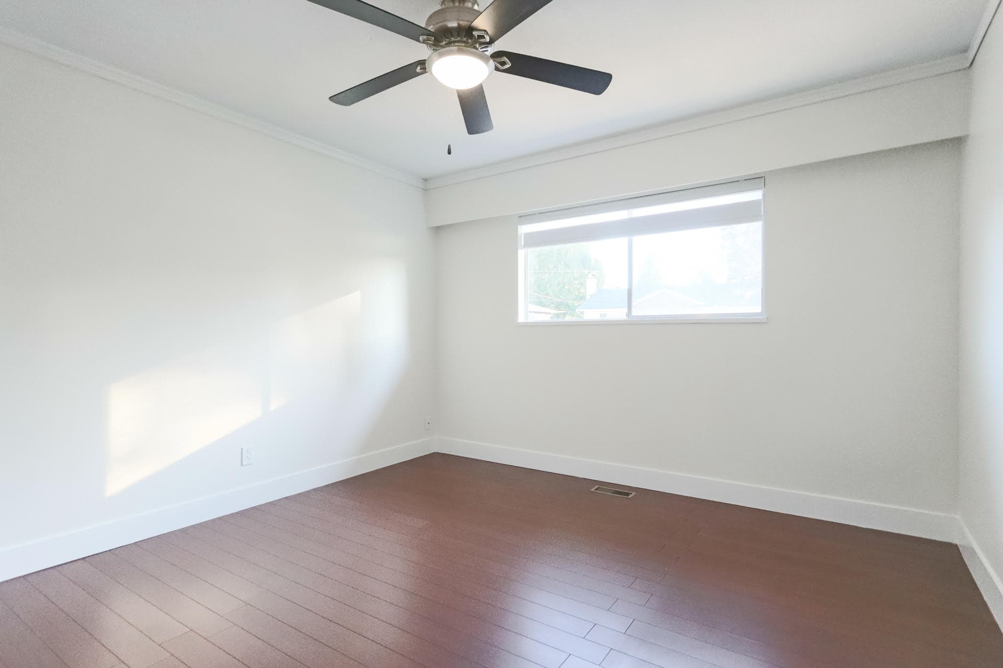 Upstairs room featuring a ceiling fan, large window with natural light, white walls, and hardwood flooring in a residential property.