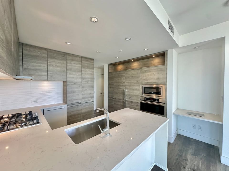 Spacious kitchen in Burnaby featuring contemporary grey cabinetry, a large island with a built-in sink, and stainless steel oven and microwave, ideal for modern living and entertaining.