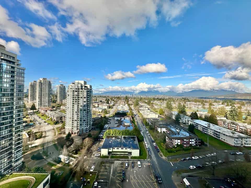 Panoramic view of Burnaby cityscape featuring tall residential towers, commercial areas, and scenic mountains in the background.