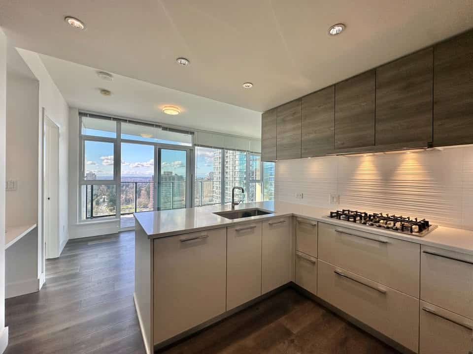 Bright and contemporary kitchen in a Burnaby condo featuring sleek cabinetry, stainless steel appliances, and large windows offering stunning cityscape views. Perfect for urban living and entertaining.