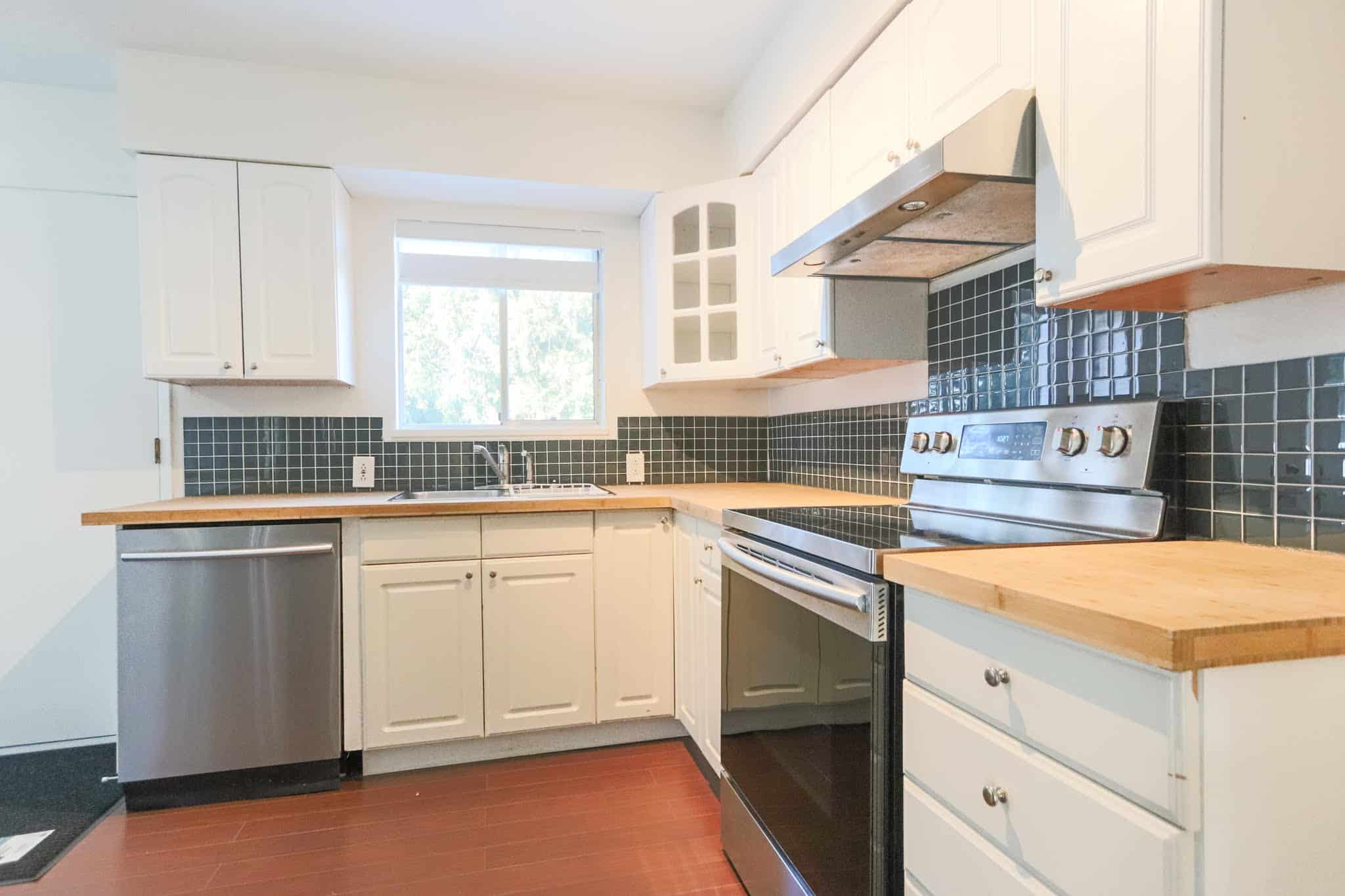 Bright kitchen featuring white cabinetry, black tiled backsplash, and stainless steel appliances.