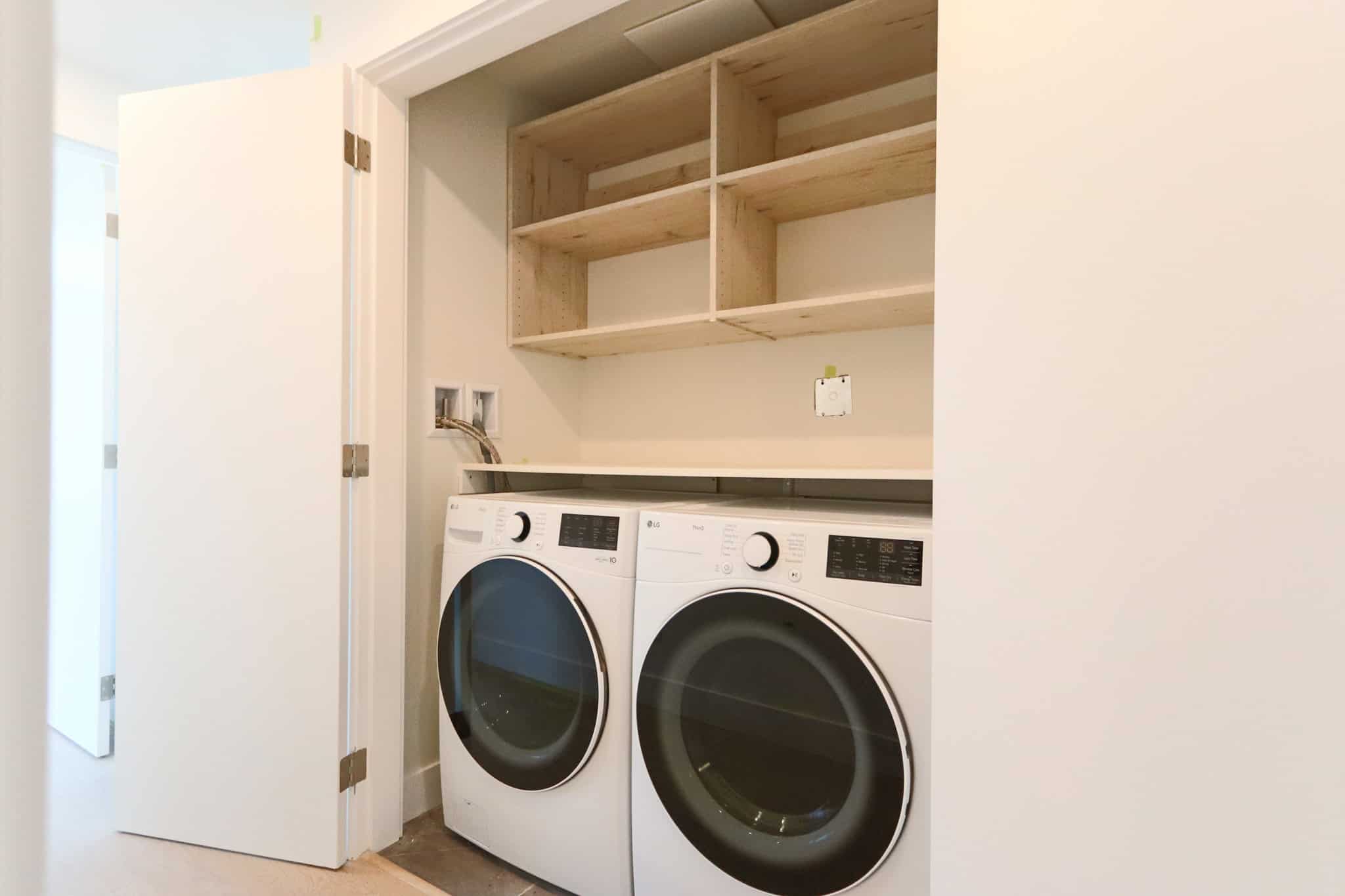 Bright laundry area featuring modern washer and dryer units with open shelving for storage in a West Vancouver residence.