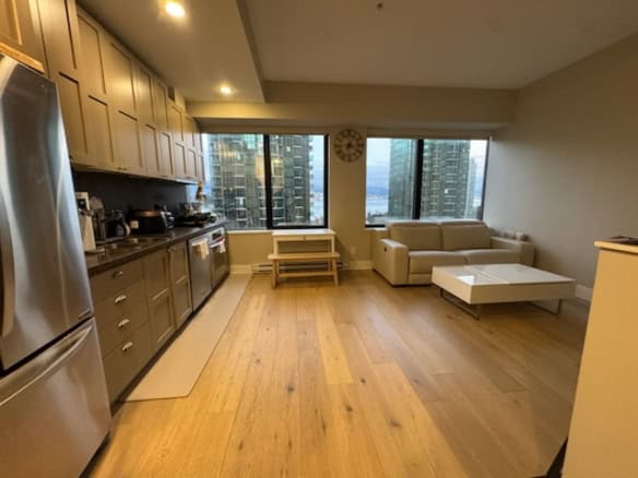 Spacious Vancouver apartment featuring a contemporary kitchen, large windows with city skyline views, and a cozy living area, ideal for urban living at 705-1333 West Georgia Street.