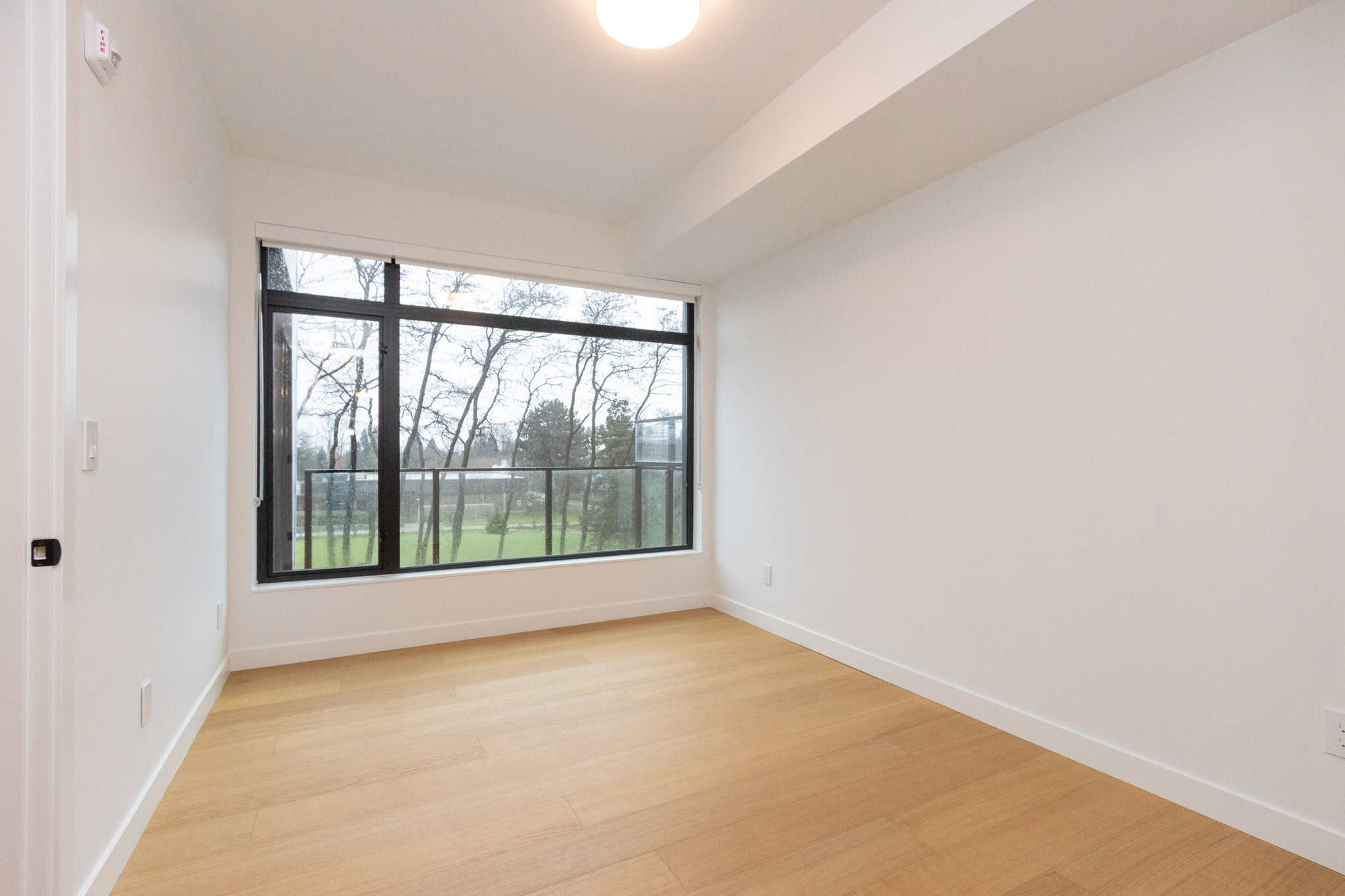 Bright, empty living room in Vancouver condo with large window and hardwood floors, ideal for homebuyers seeking a stylish property at 405-6485 Manitoba Street.