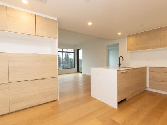 Spacious kitchen featuring sleek wooden cabinets, a white island, and large windows providing ample natural light in Vancouver.