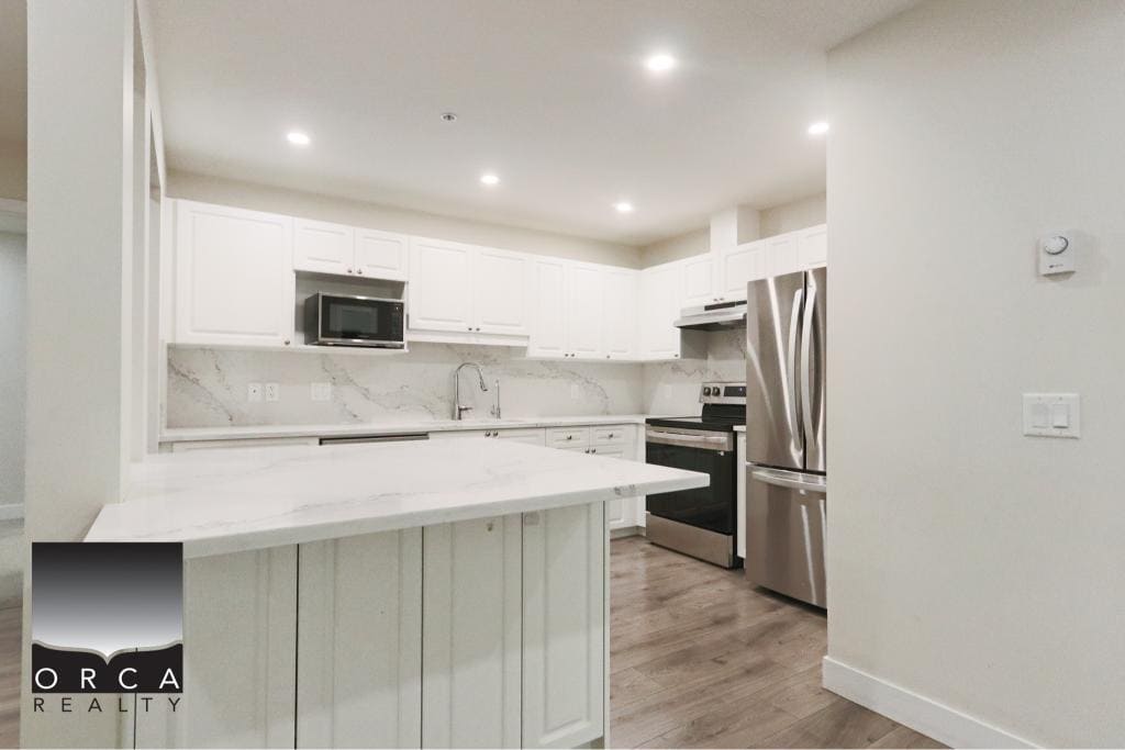 Bright and spacious kitchen in Surrey featuring stainless steel refrigerator, oven, microwave, and white cabinetry. Perfect for family living and entertaining.