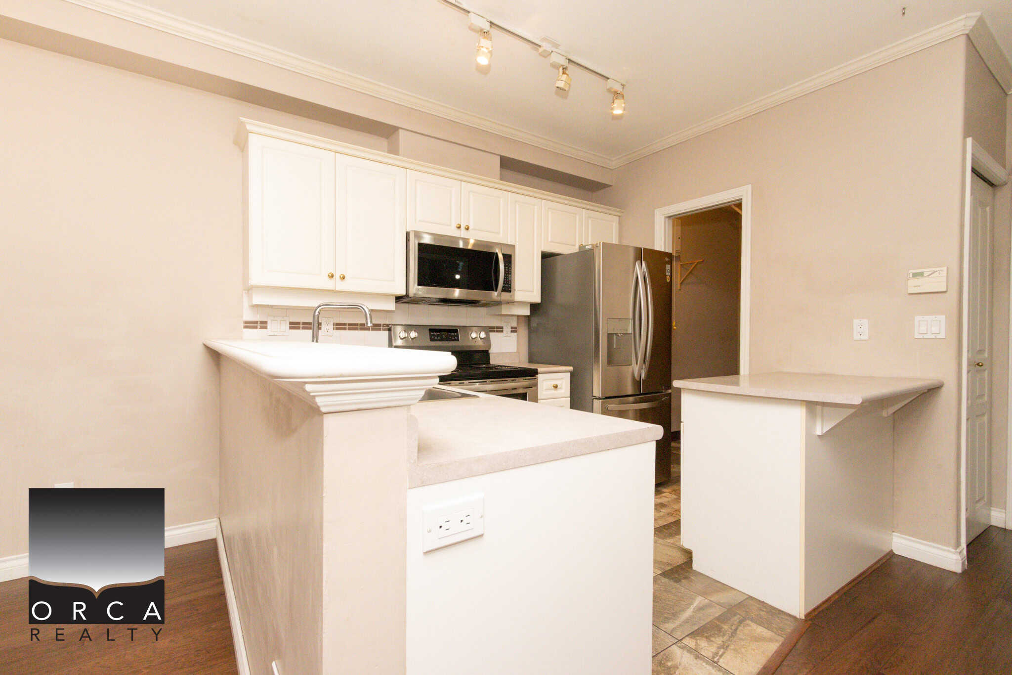 Bright kitchen featuring white cabinetry, stainless steel appliances, and a cozy breakfast bar in Coquitlam. Perfect for family living and entertaining.