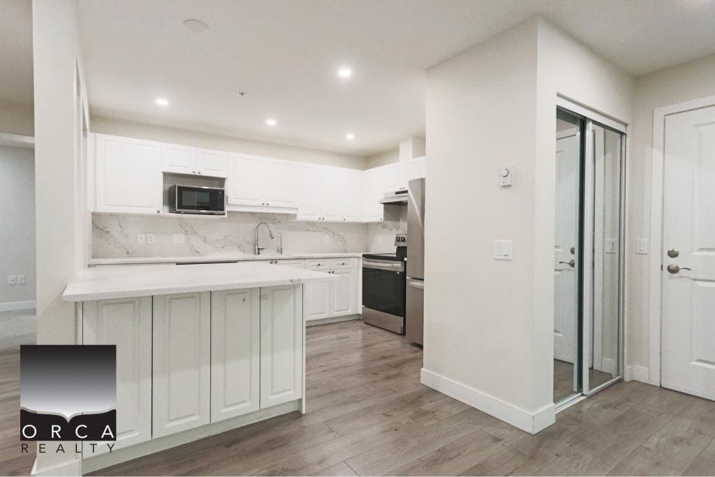 Bright, open-concept kitchen featuring white cabinetry, marble backsplash, and stainless steel appliances in Surrey. Perfect for modern living and entertaining.