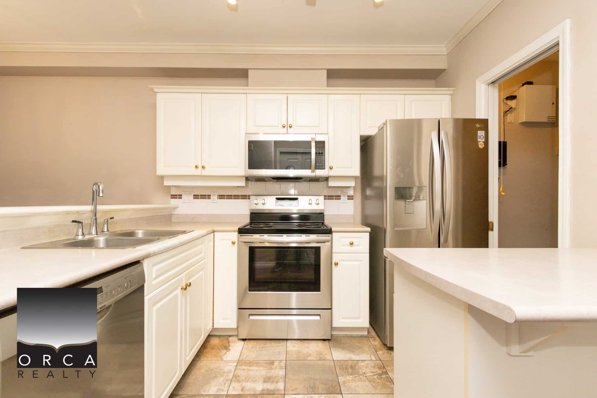 Spacious kitchen in Coquitlam featuring stainless steel refrigerator, oven, microwave, and white cabinetry, perfect for family living and entertaining.
