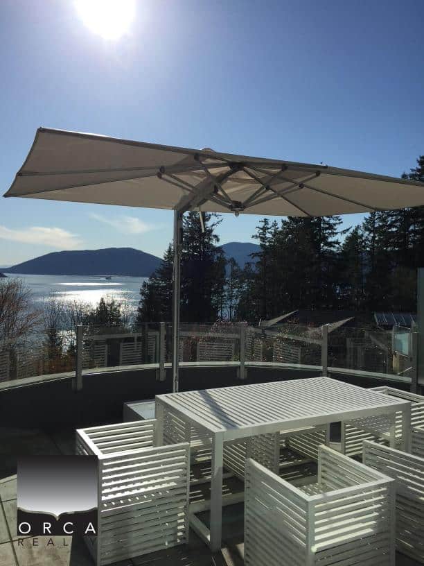 Outdoor patio setup with large umbrella, white furniture, and scenic water and mountain background.